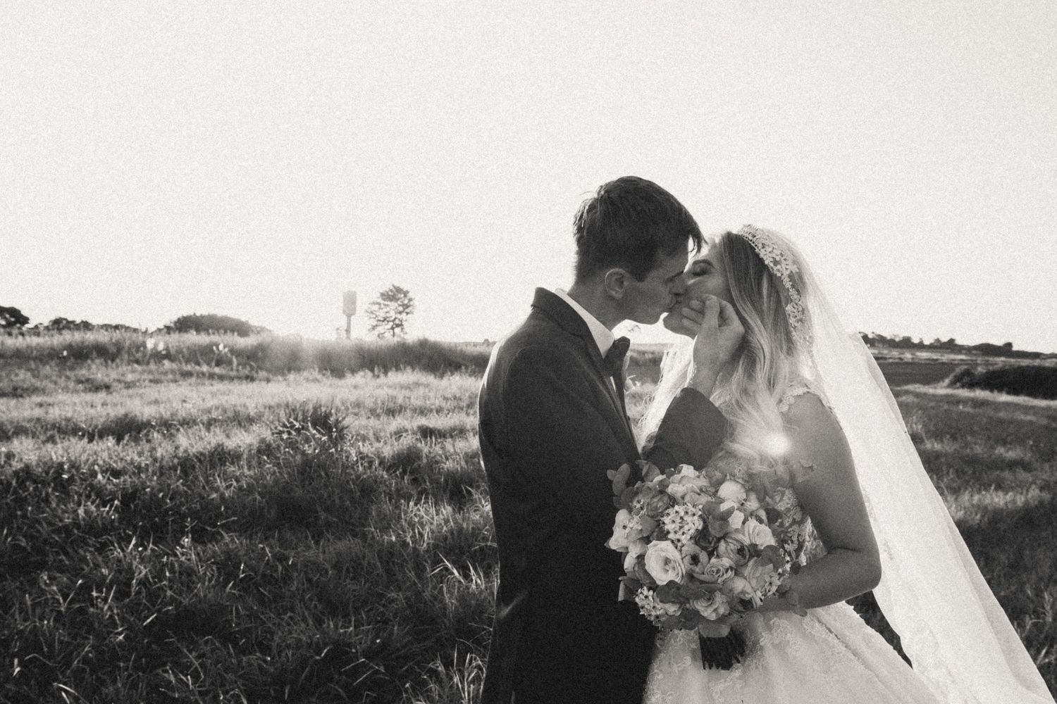 Romantic black and white photo of newlyweds embracing in a sunset field.