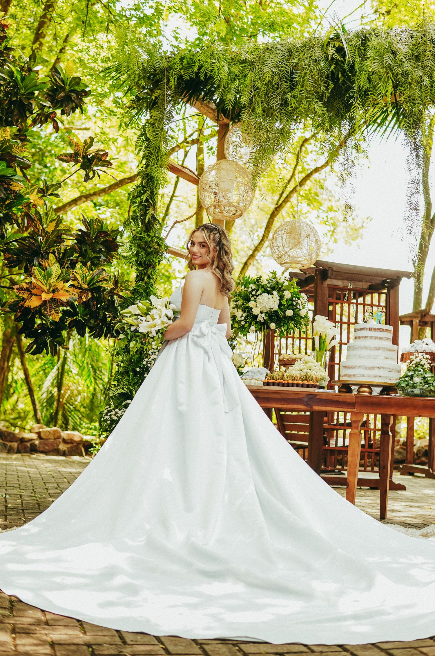 A stunning white wedding dress with long train photographed in a lush garden setting with wooden deck and greenery overhead.
