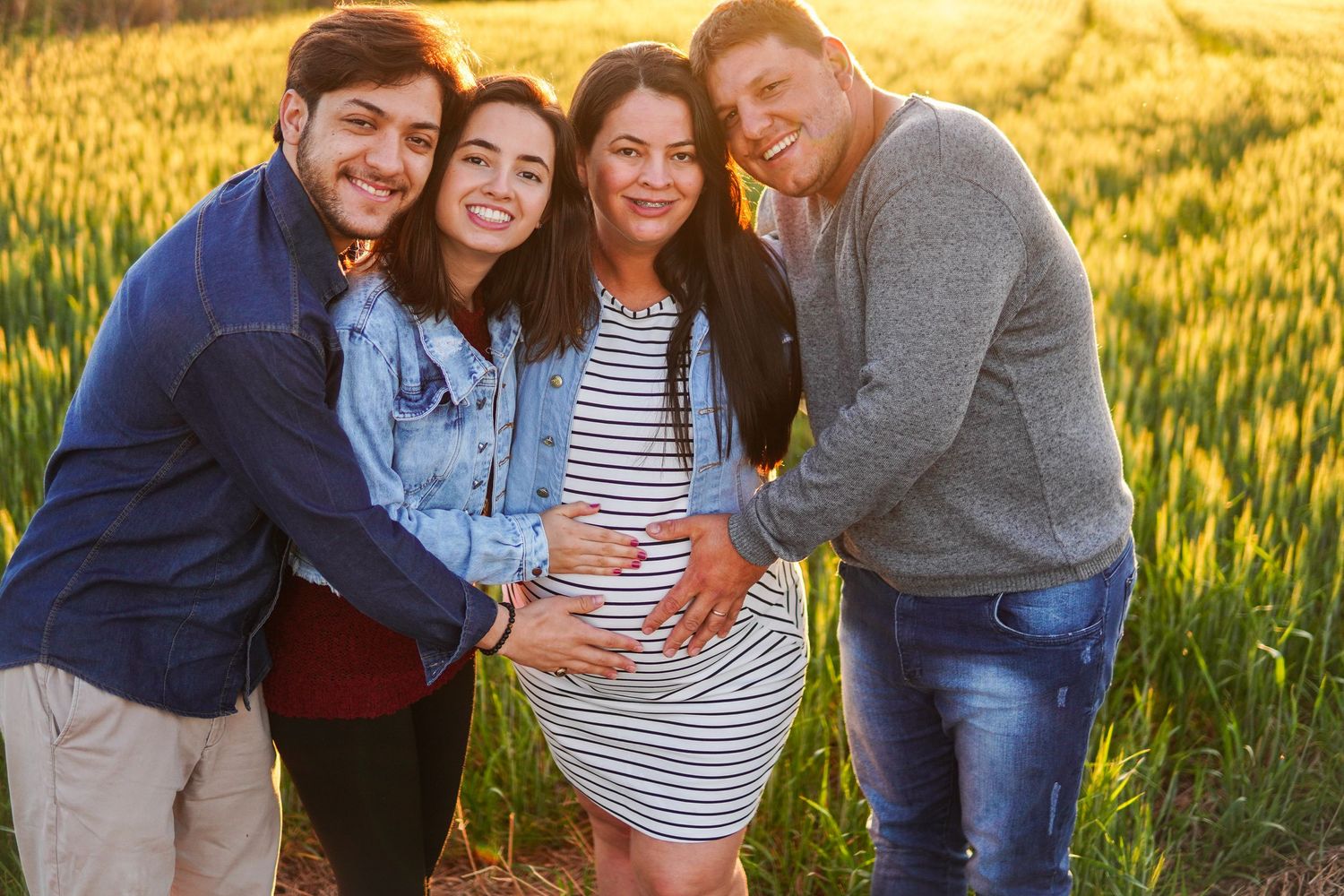Friends gather around expectant mother for sunset pregnancy announcement in wheat field.