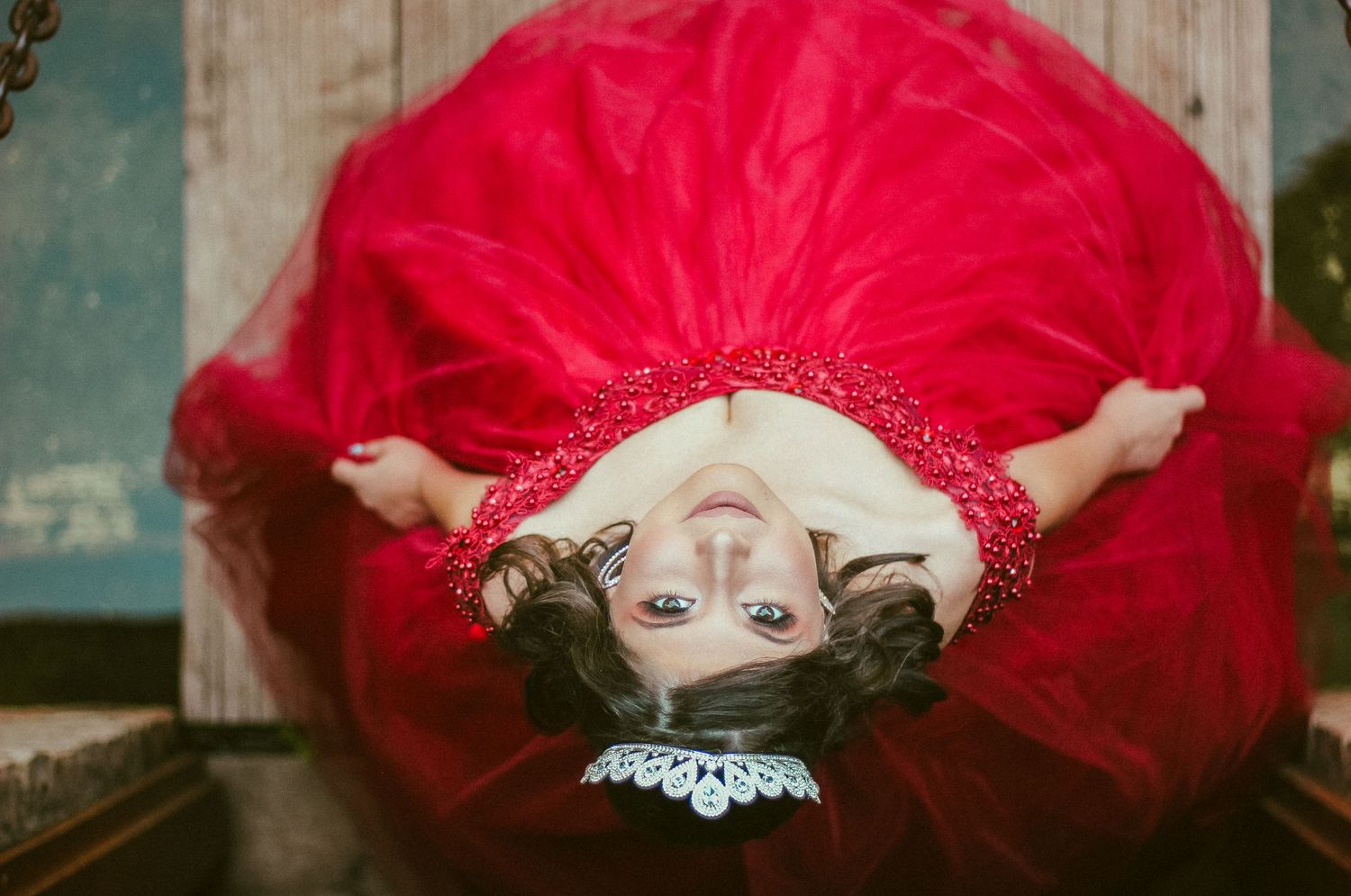 A red tulle dress with glitter trim spreads out dramatically on a wooden floor in a vintage setting.