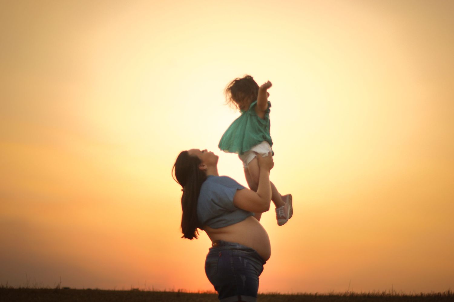 Silhouette of a pregnant woman against a warm golden sunset backdrop.
