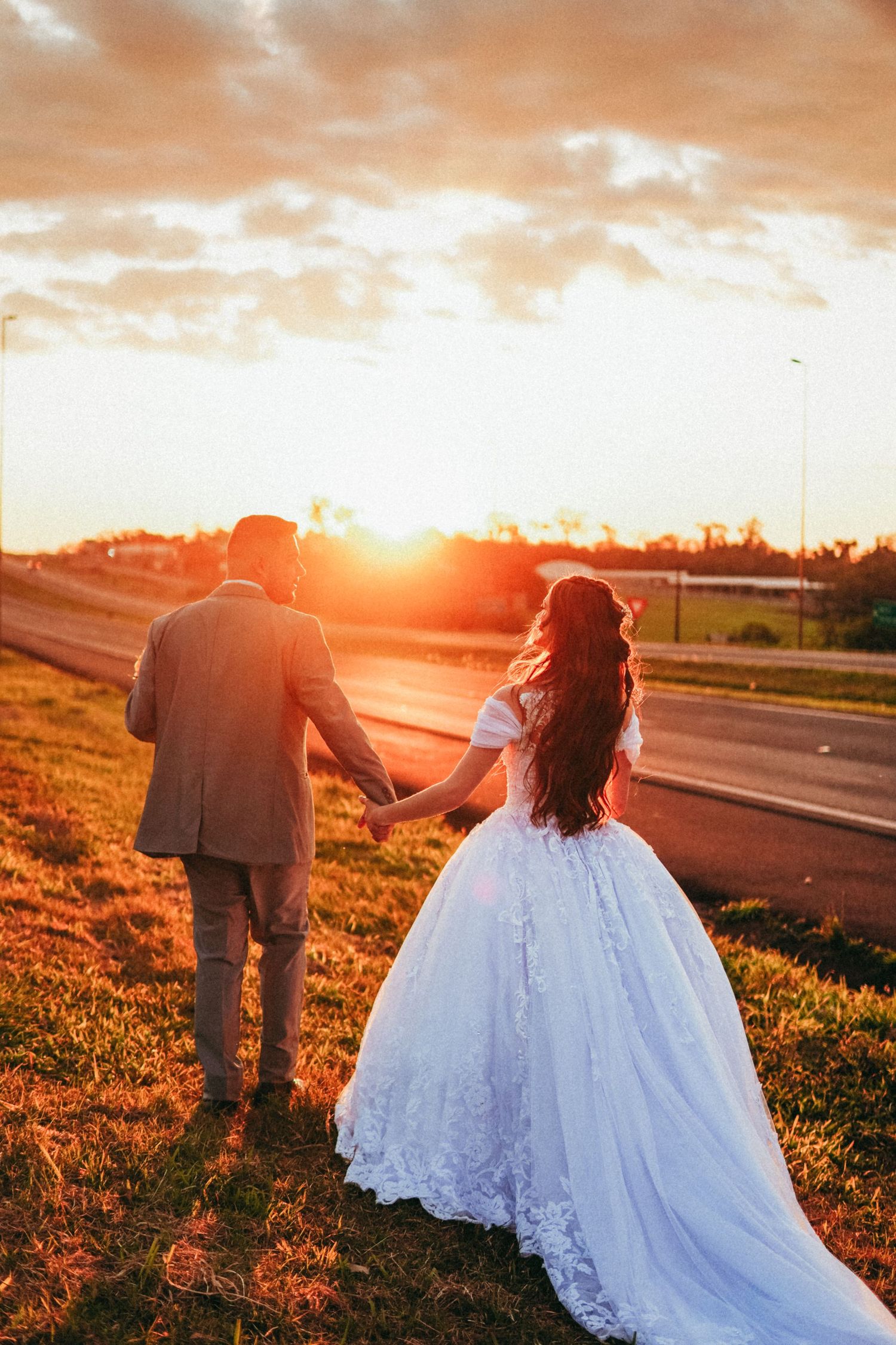 Wedding couple walks hand in hand during dramatic sunset with orange sky.