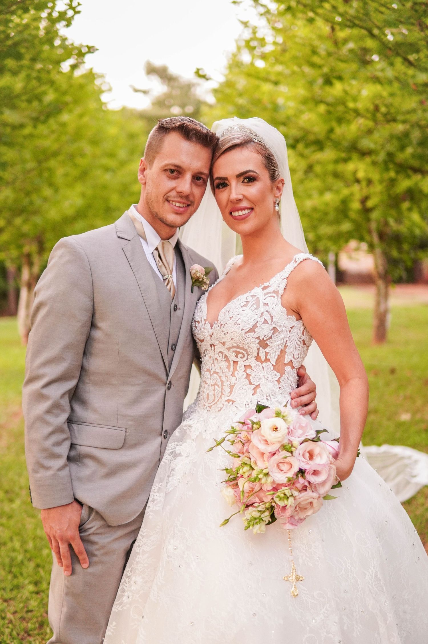 Spring wedding portrait with couple in grey suit and lace gown holding pink bouquet.