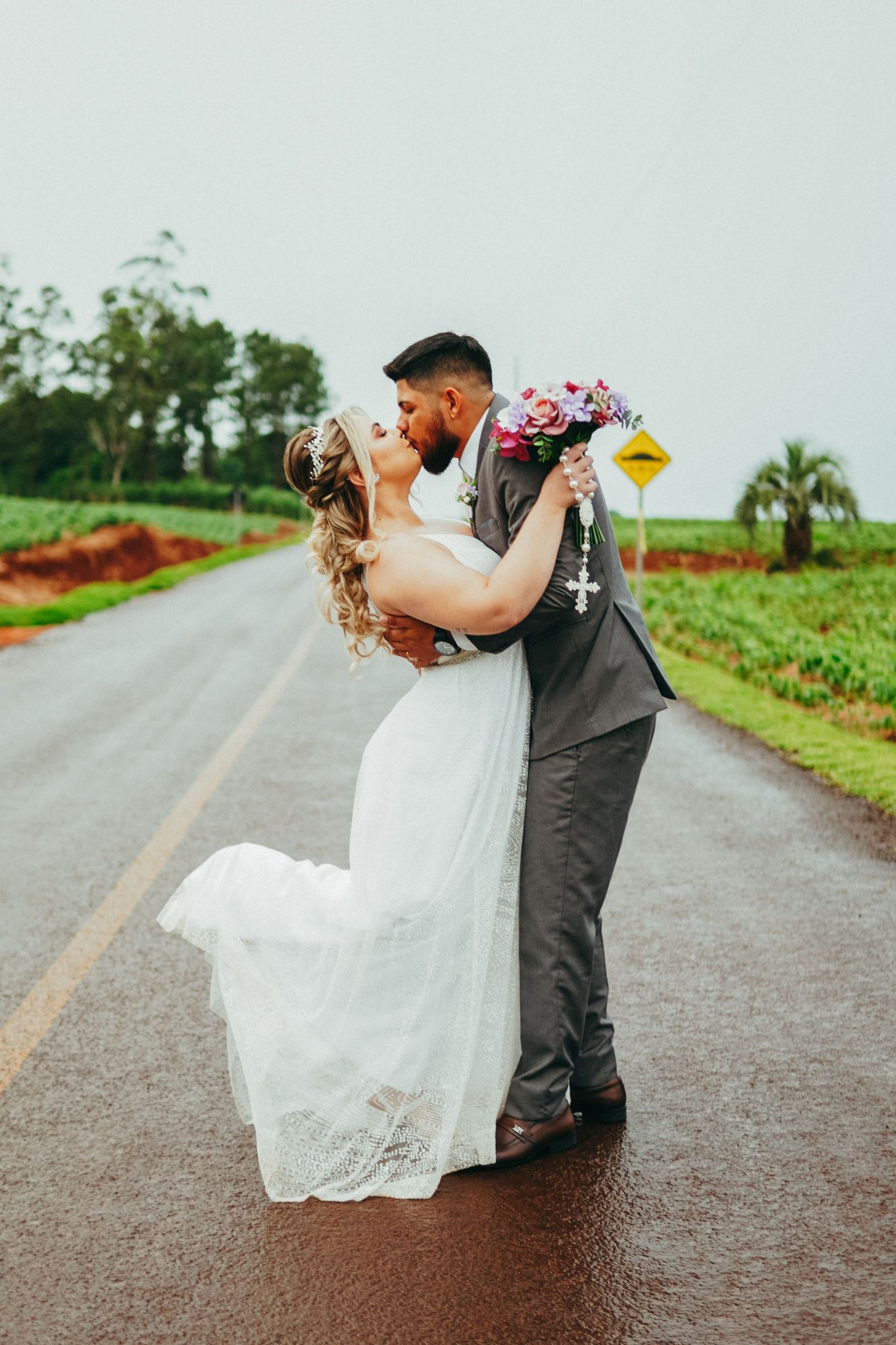 Romantic newlyweds share an intimate embrace on a rural road with lush greenery in the background.