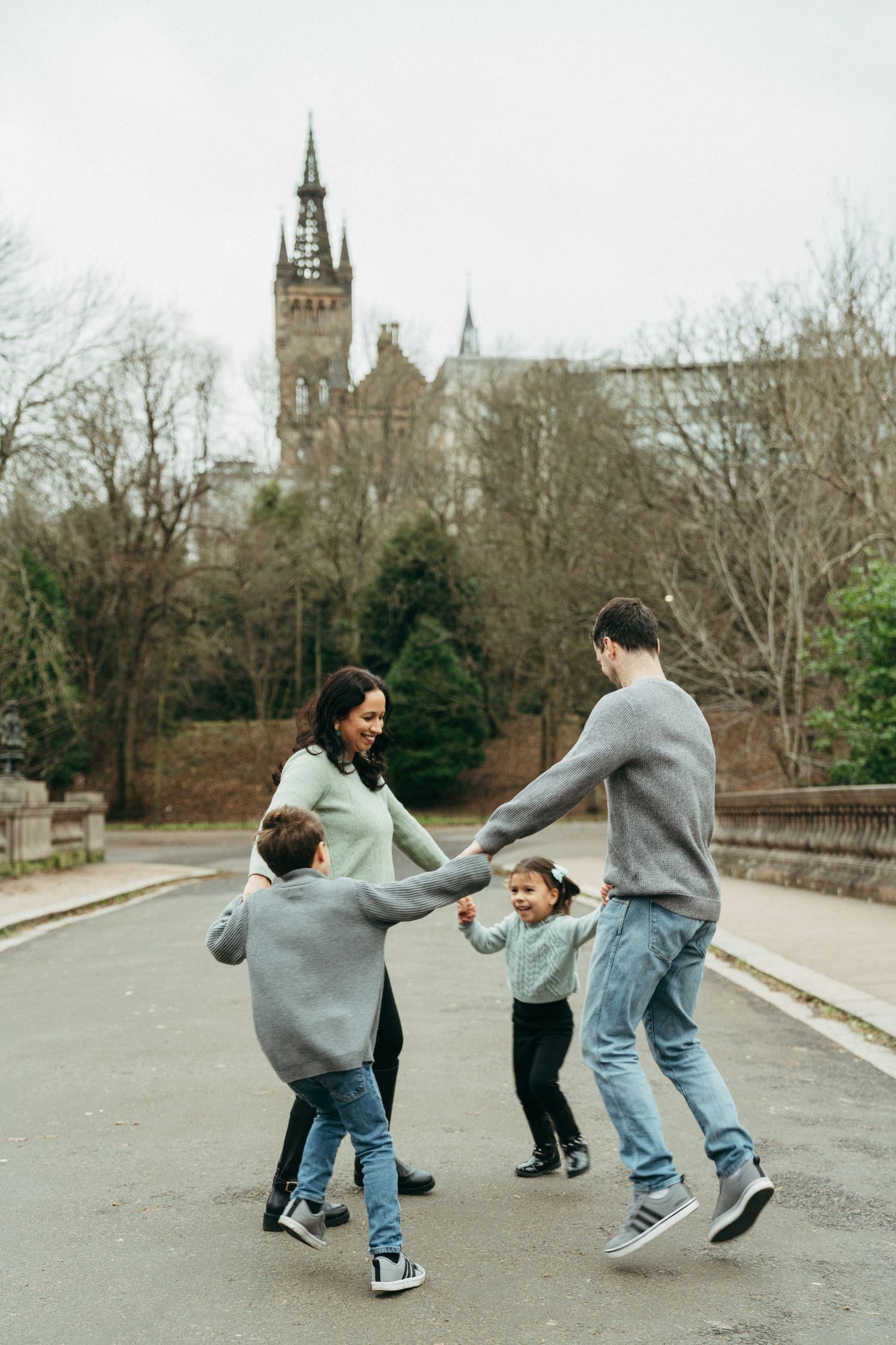 Family of four joyfully holding hands in a circle outdoors, with a historic castle building visible in the background.