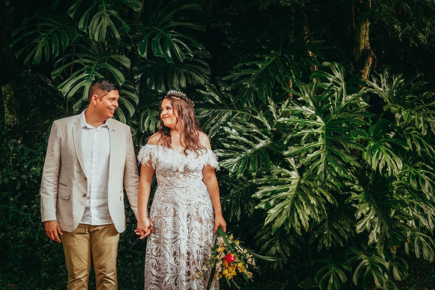 Wedding couple poses in front of lush tropical greenery during intimate beachside ceremony in Hawaii.