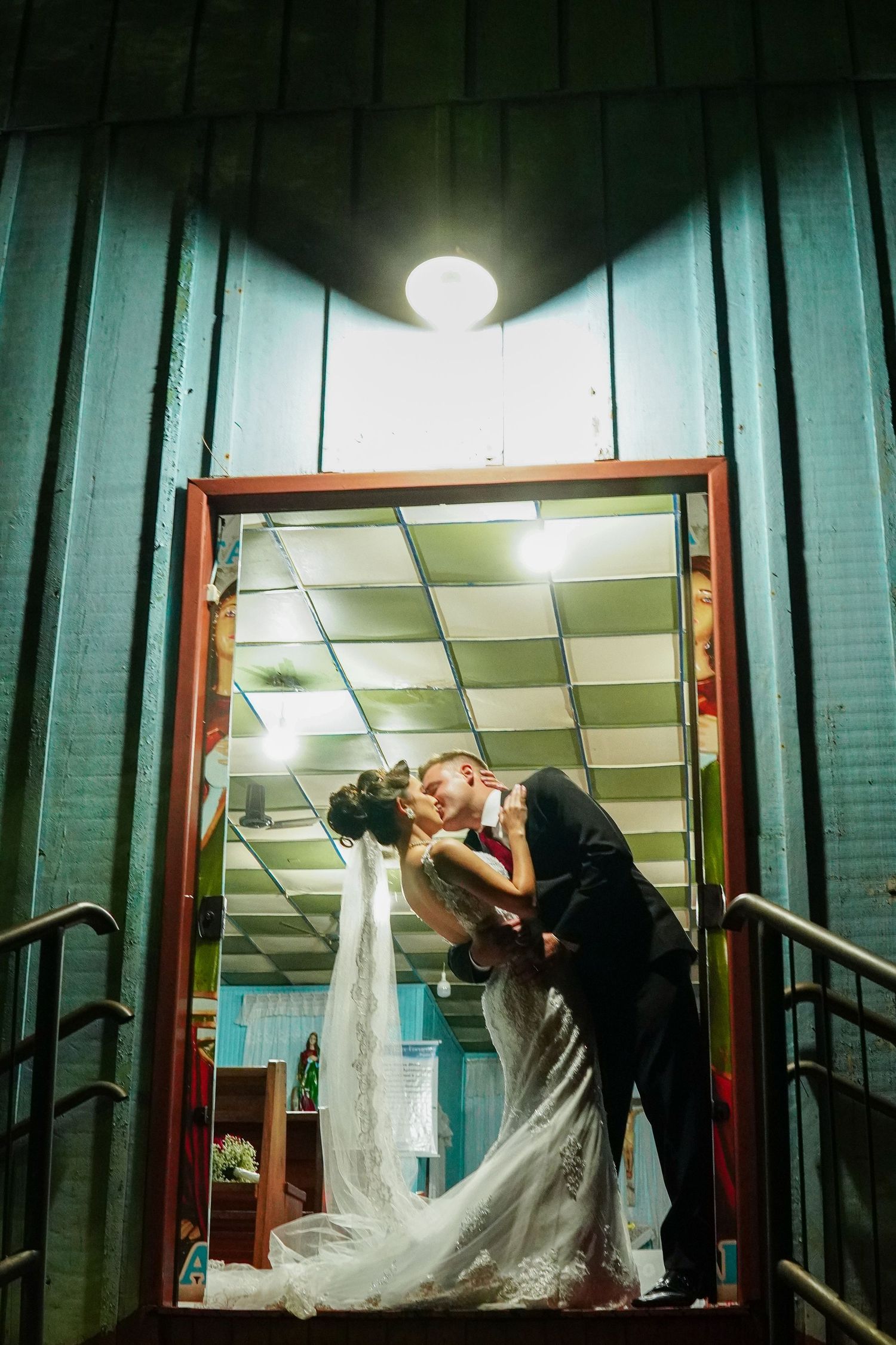 Dramatic nighttime wedding photo of couple kissing in a doorway with overhead lighting.