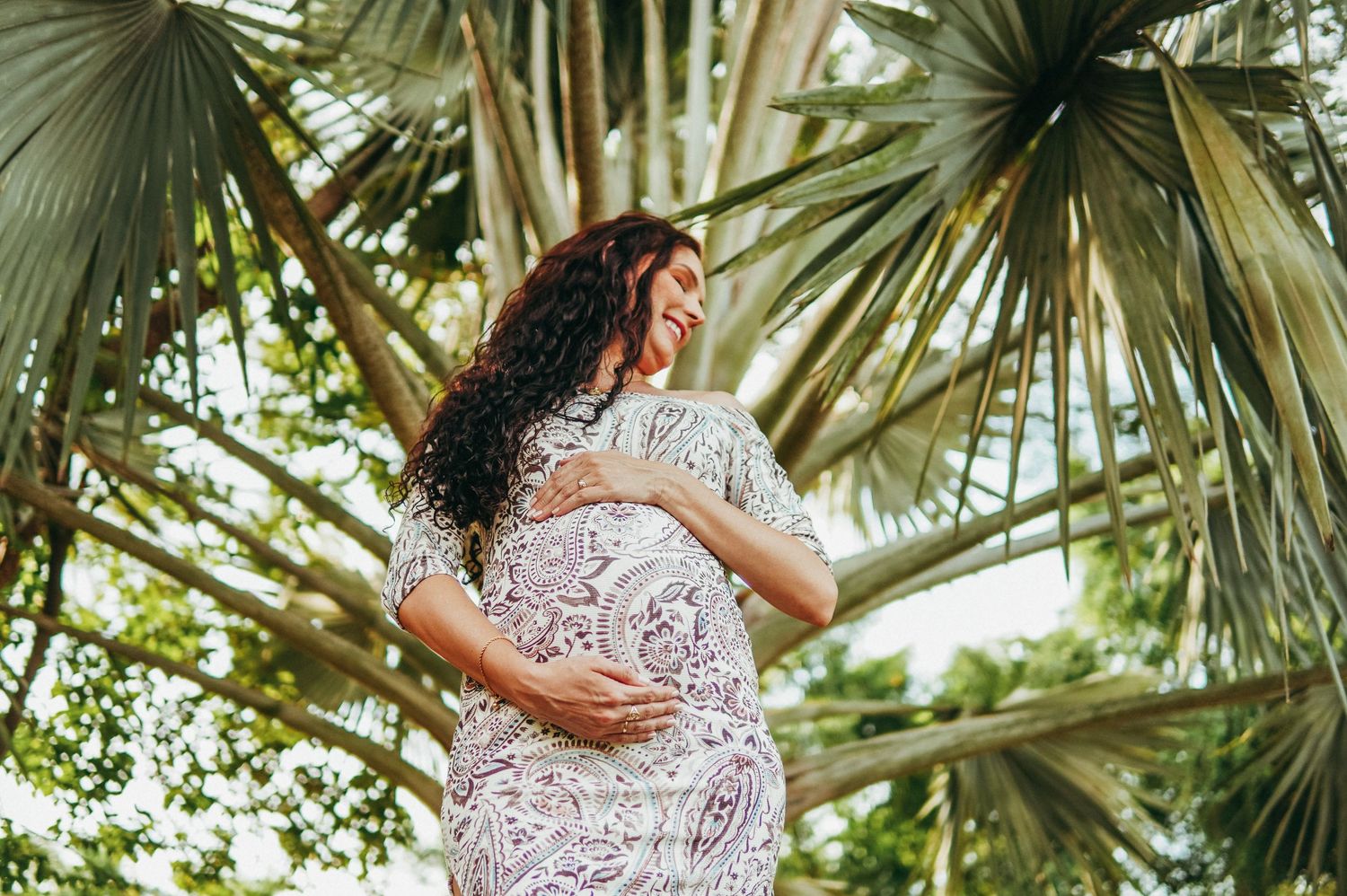 Multiple shots of woman in white lace dress posing under tropical palm leaves.