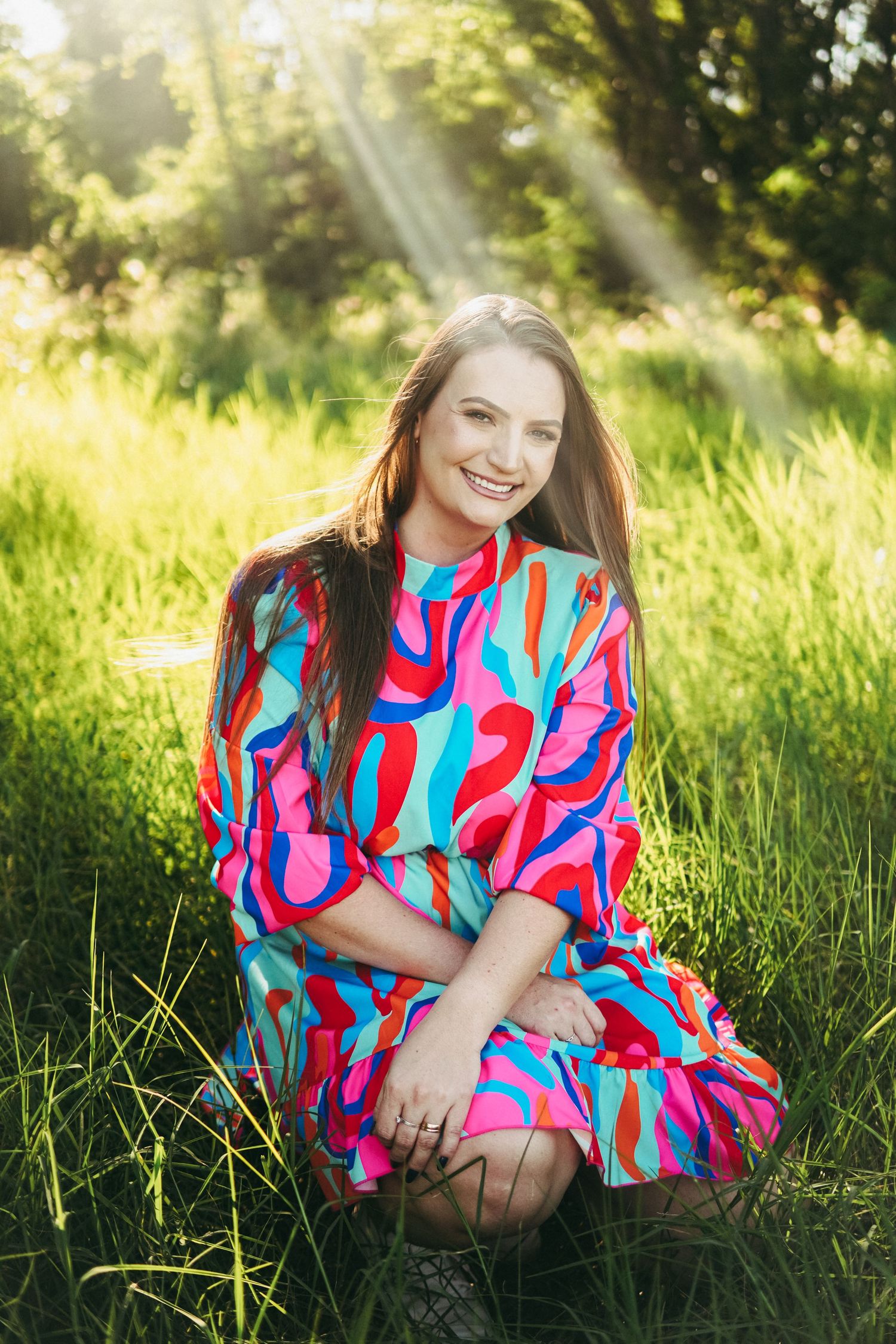 A vibrant pink and blue patterned dress stands out against a sunlit grassy meadow on a summer evening.