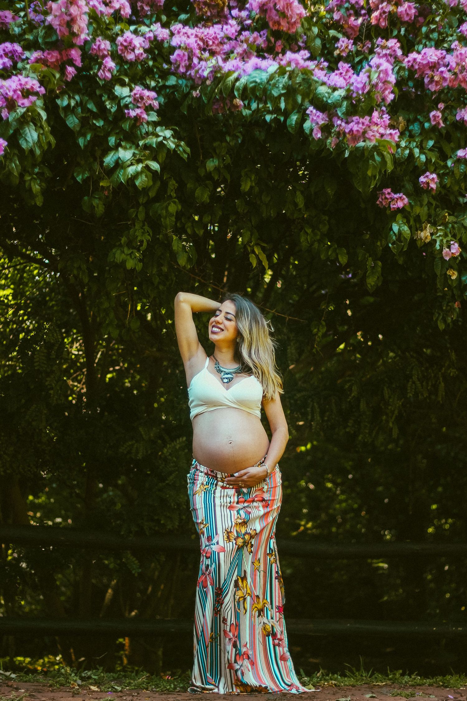 Maternity photos in a garden with blooming pink flowers creating a romantic backdrop.
