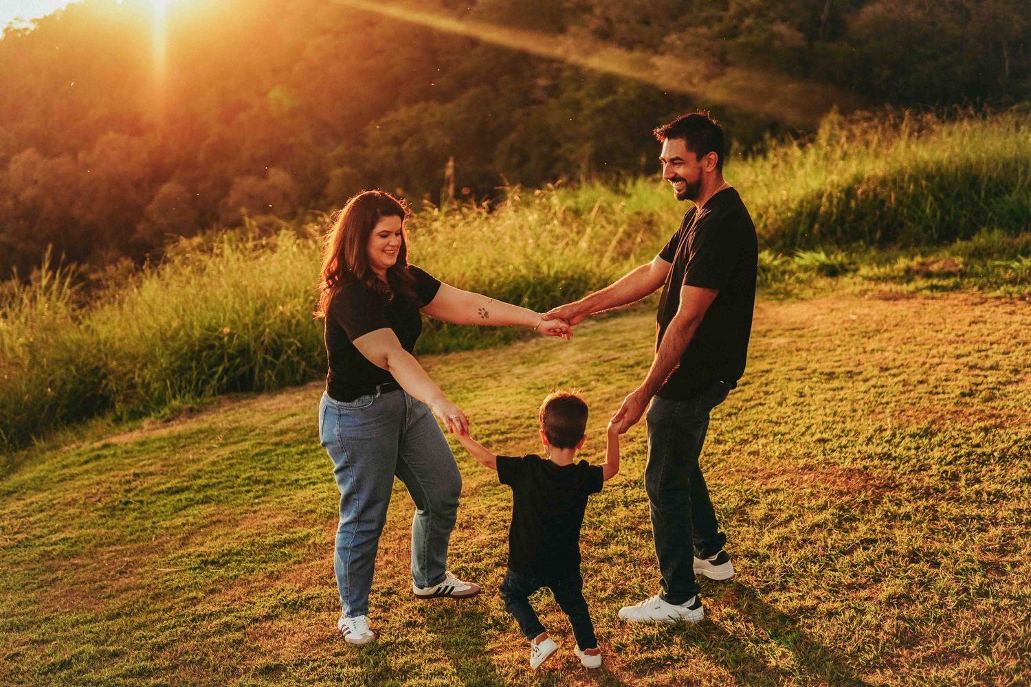 Playful family portraits captured at golden hour in an outdoor grassy field.