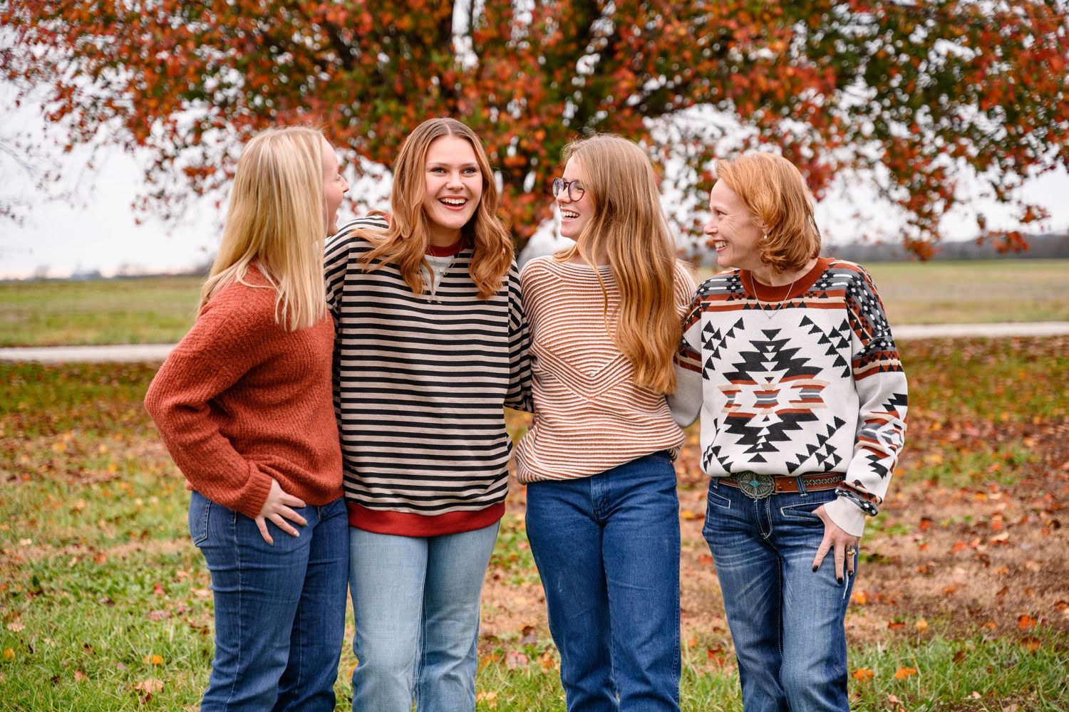 A group of family in coordinating fall outfits stand together outdoors among autumn leaves.