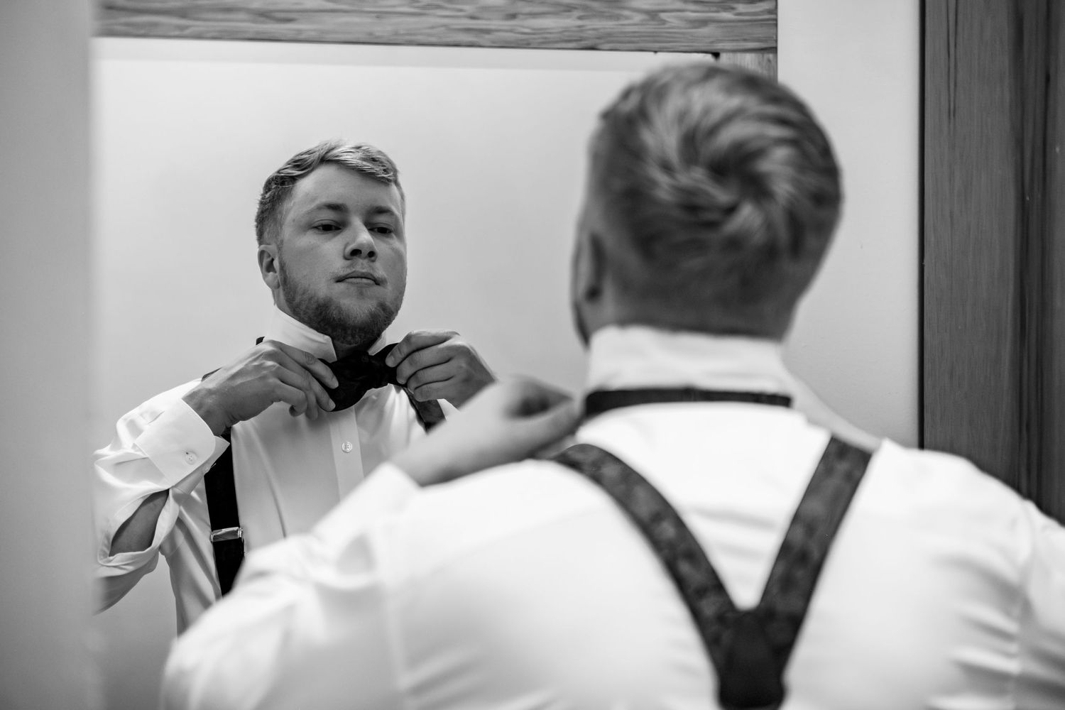 A groom adjusting his tie while getting ready for his wedding in Arkansas.