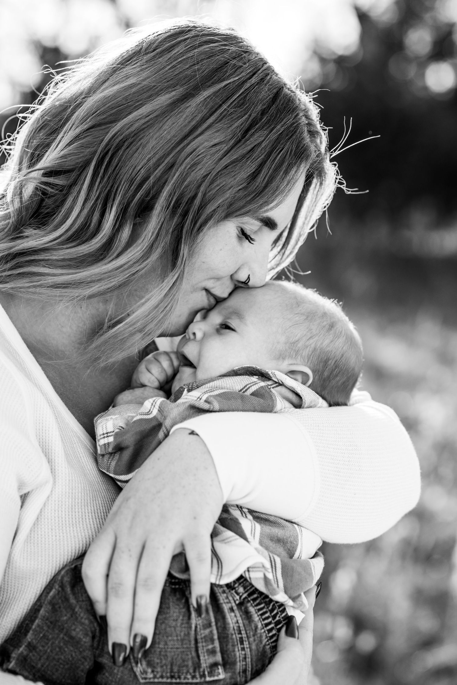 A mother and her newborn child share a sweet moment in an open field.