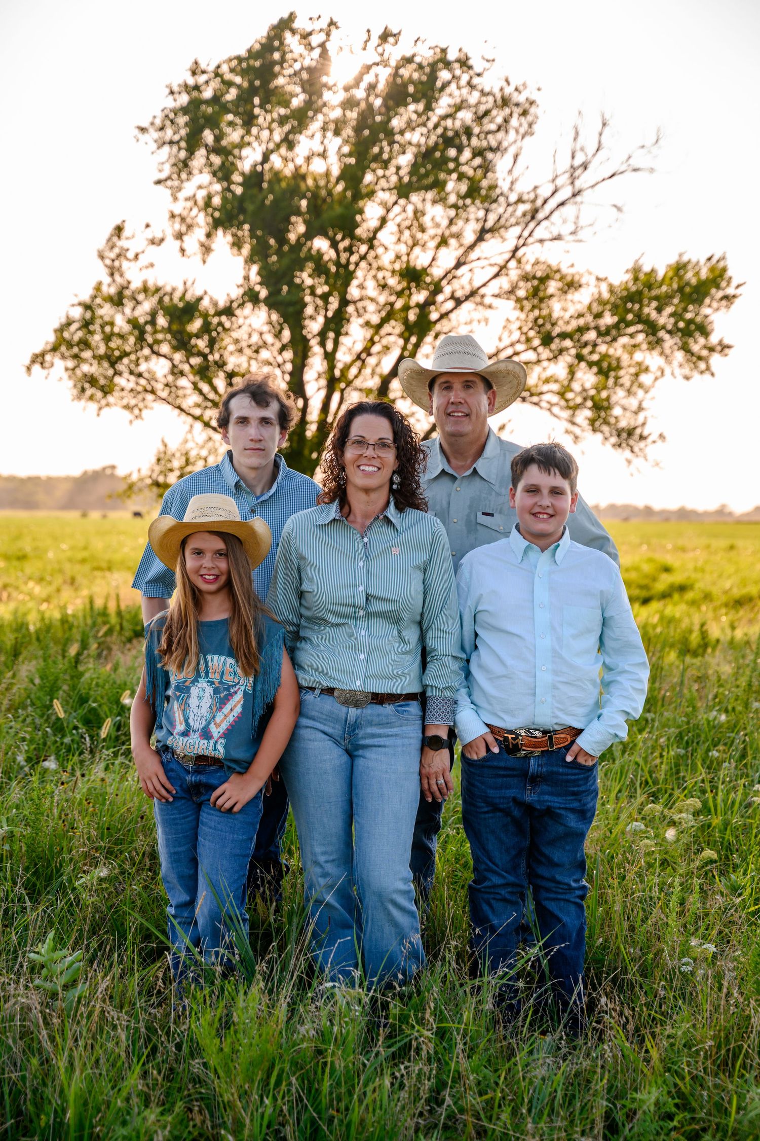 Family in denim clothing poses together in a golden field at sunset in Southeast Kansas.