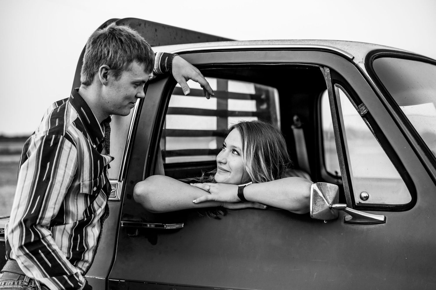A girl sitting in the truck, leaning against the window, staring into her boyfriend's eyes.