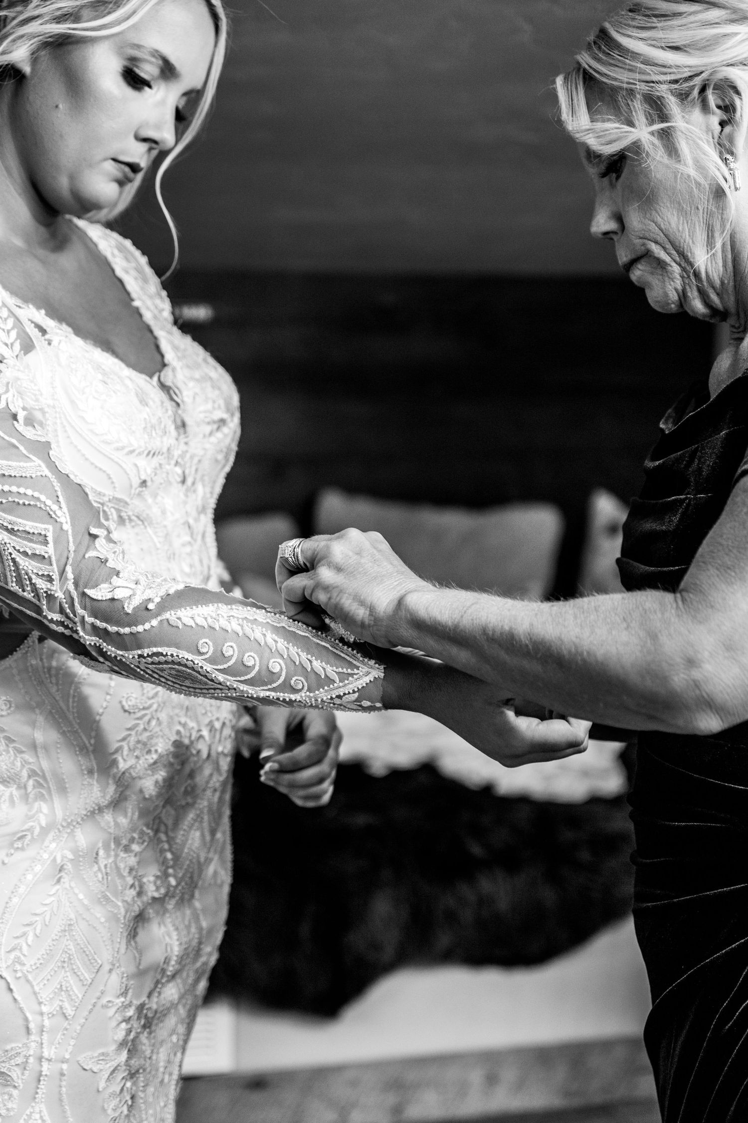 Final adjustments are being made to an intricate lace wedding dress sleeve by the bride and her mother.