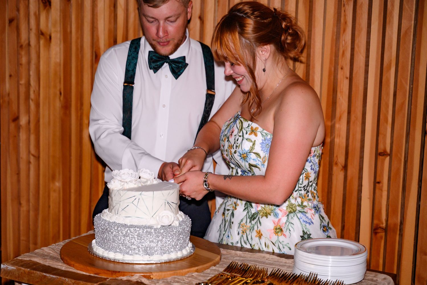 A couple cuts their white wedding cake together at a rustic wooden venue during their reception.