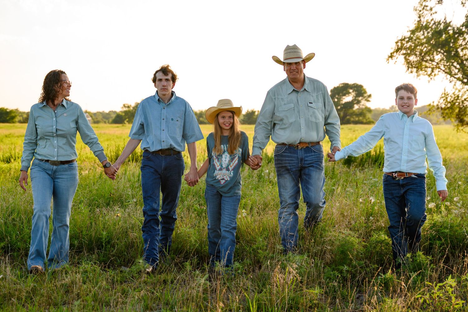 A family in western attire walks together through a sunlit meadow at golden hour, captured in a panoramic style.