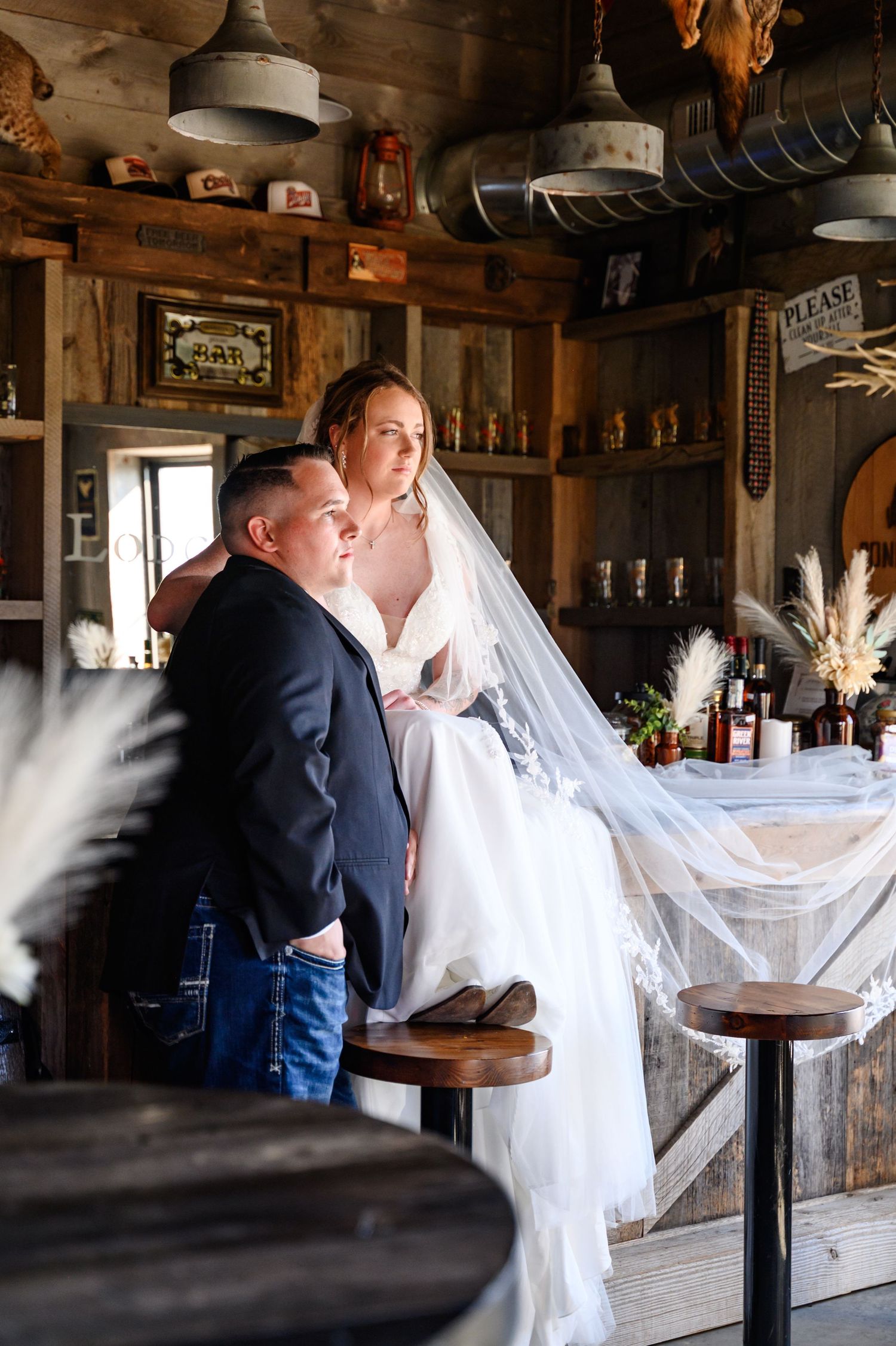 A bride and groom share an intimate moment in a rustic wooden barn setting with flowing white veil details.