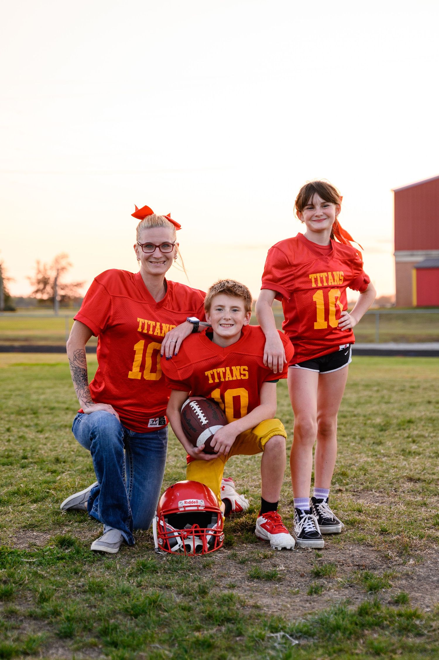 Family members in red Titans jerseys pose together on a grass field at sunset for sports-themed milestone photos.