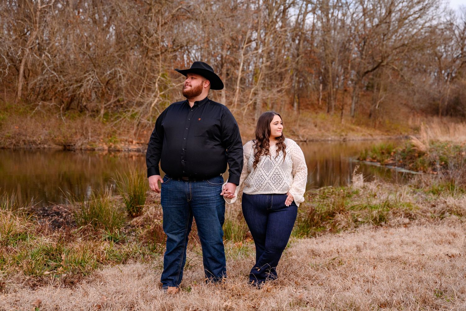 A couple looking off into the distance, in an open field with a pond behind them, in Southeast Kansas.
