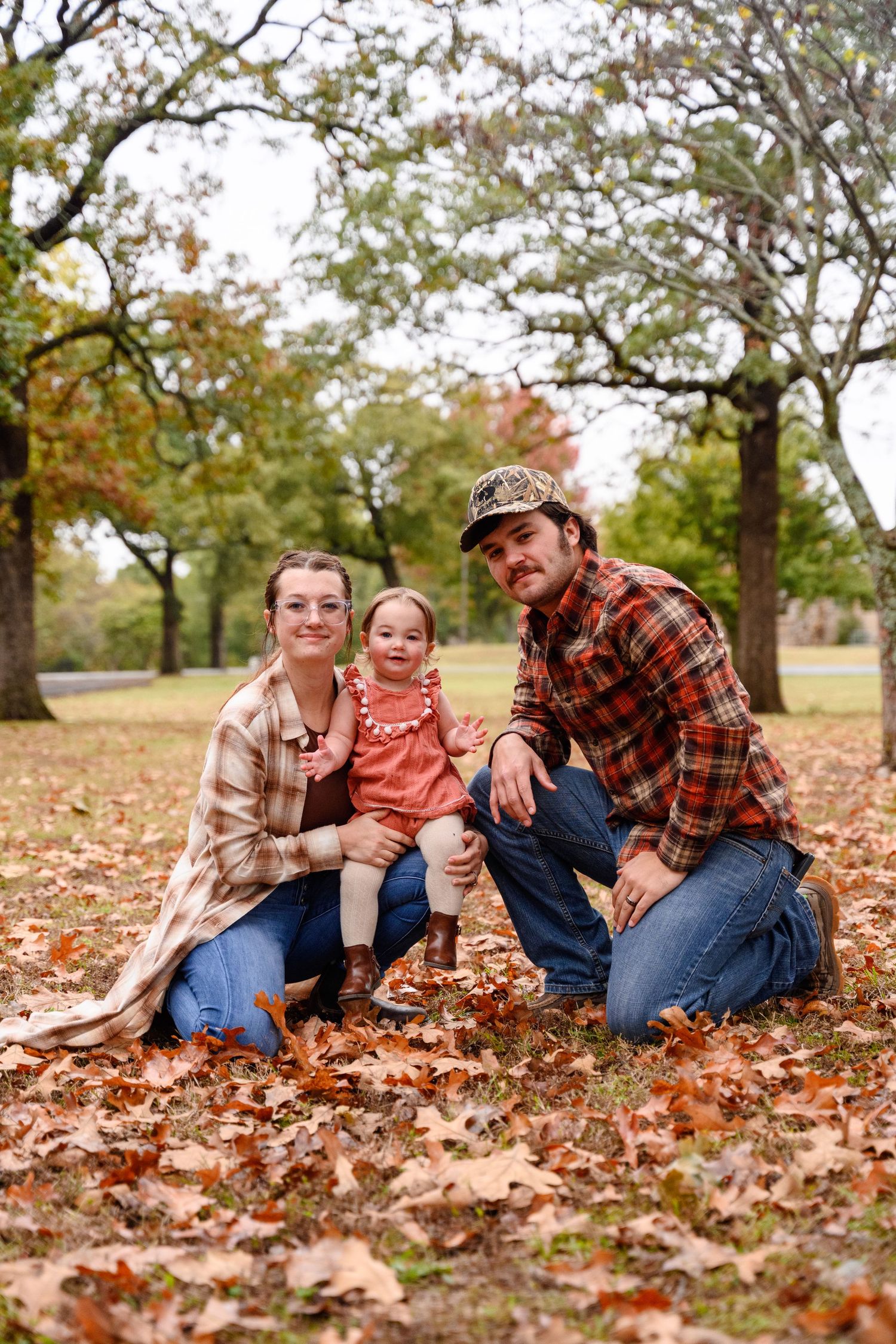 Family sitting together on fallen autumn leaves in a park during a fall mini session in Kansas.