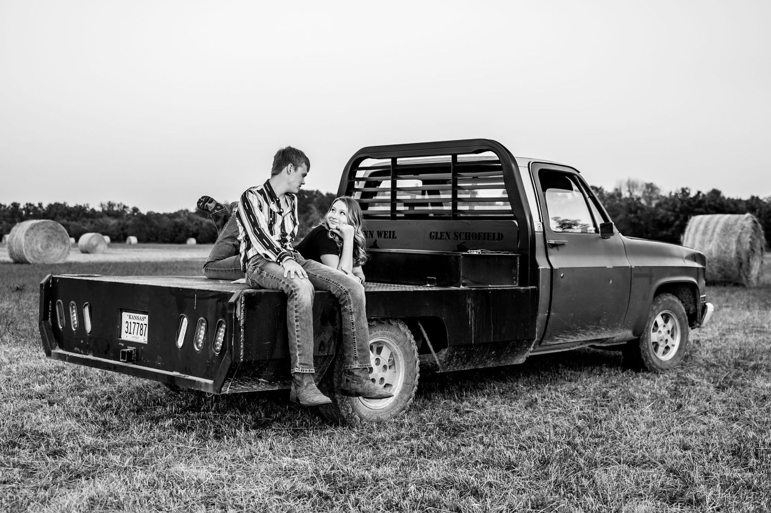 A couple sitting on a flatbed pickup truck in a Kansas field with hay bales in the background.