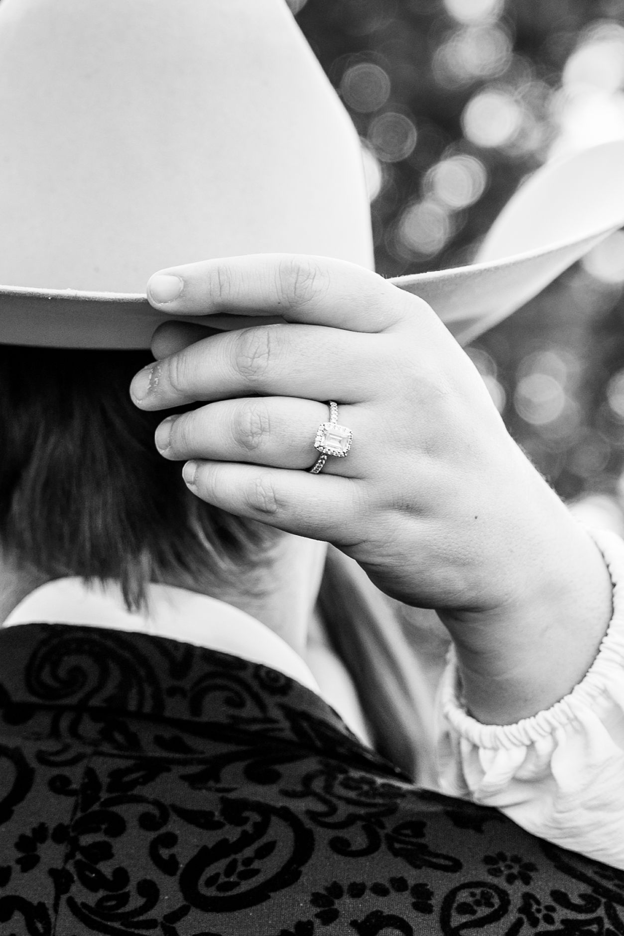 A close-up of a woman's engagement ring resting on her fiancé's cowboy hat.