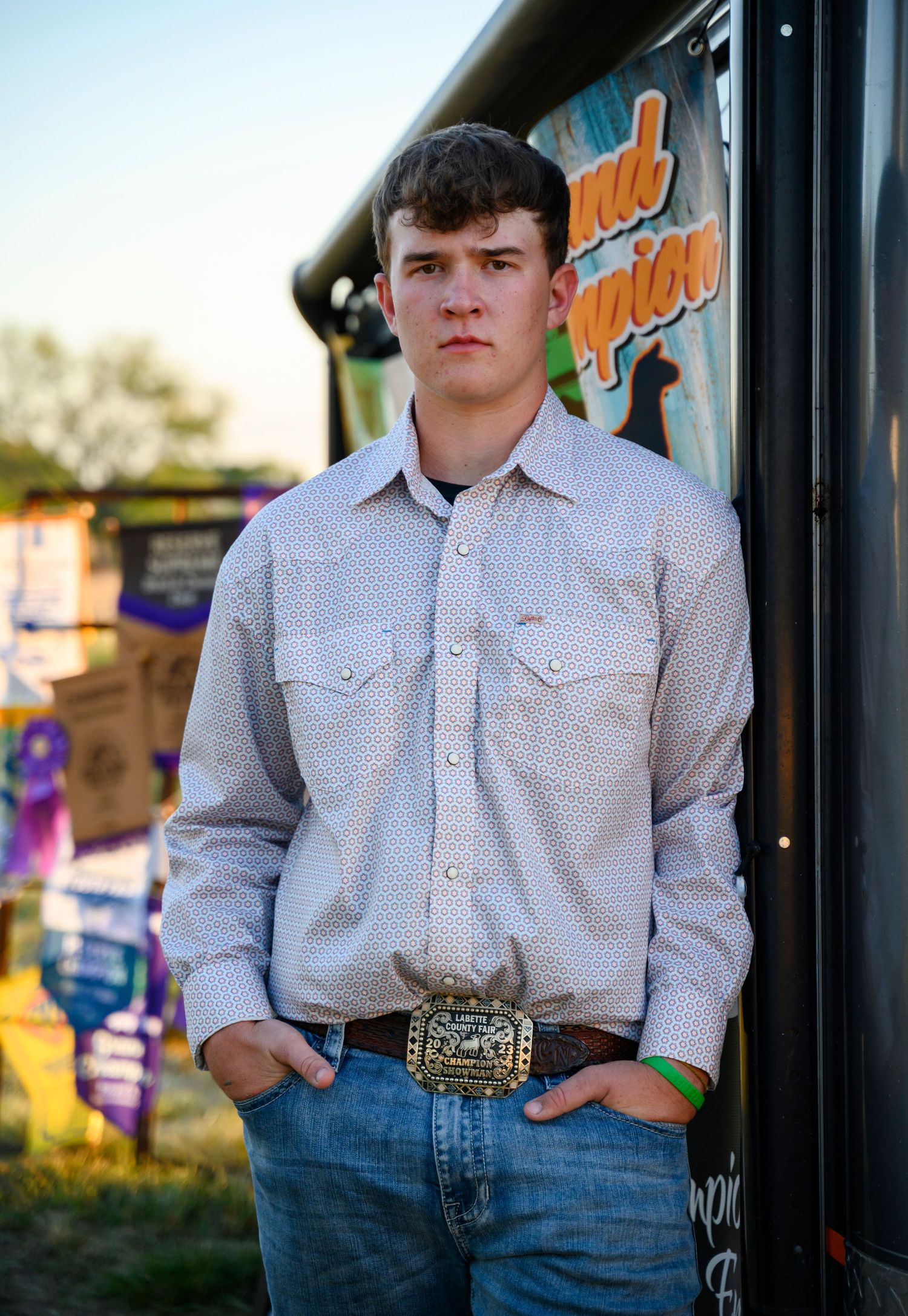 A Kansas senior is leaning against a trailer with champion banners behind him.