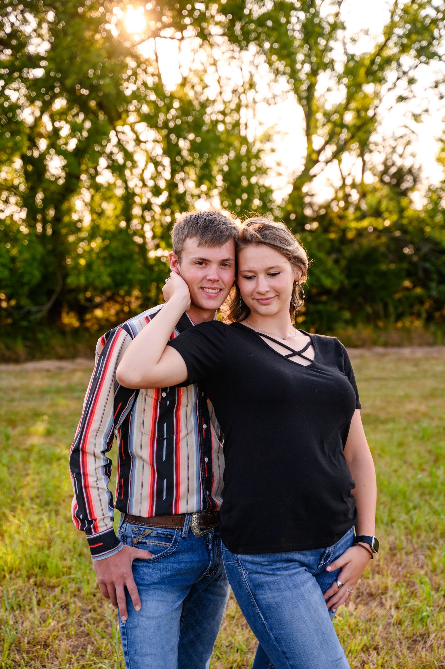 A couple shares a tender moment in a grassy field during golden hour sunset.