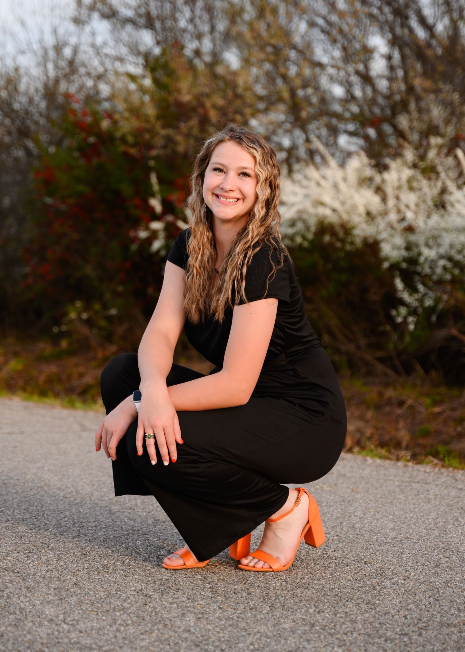 A senior girl kneeling in front of flowering bushes in Southeast Kansas.