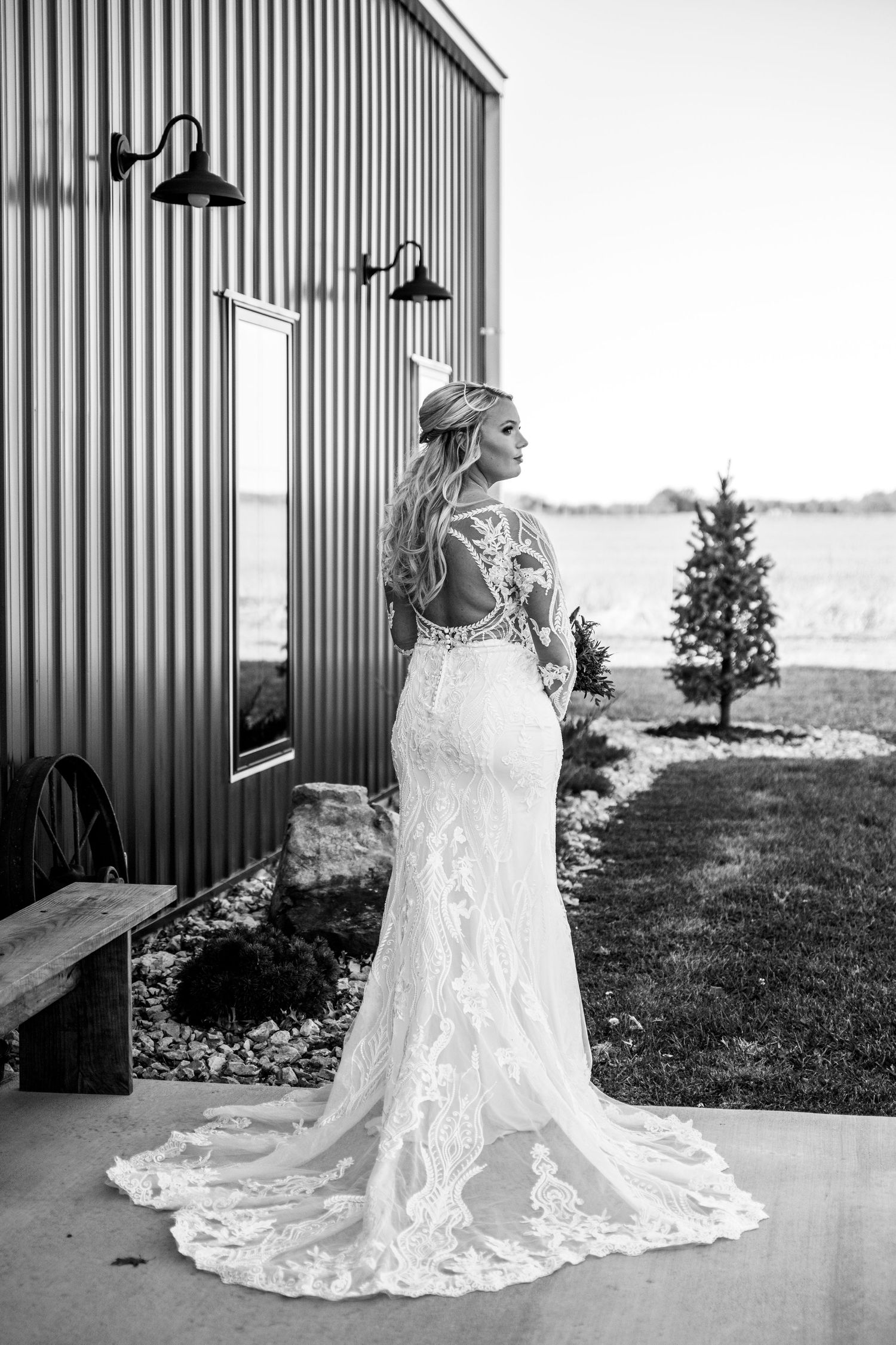 A stunning lace wedding dress with a flowing train and a beautiful bride outside of the Camp 400 wedding venue.