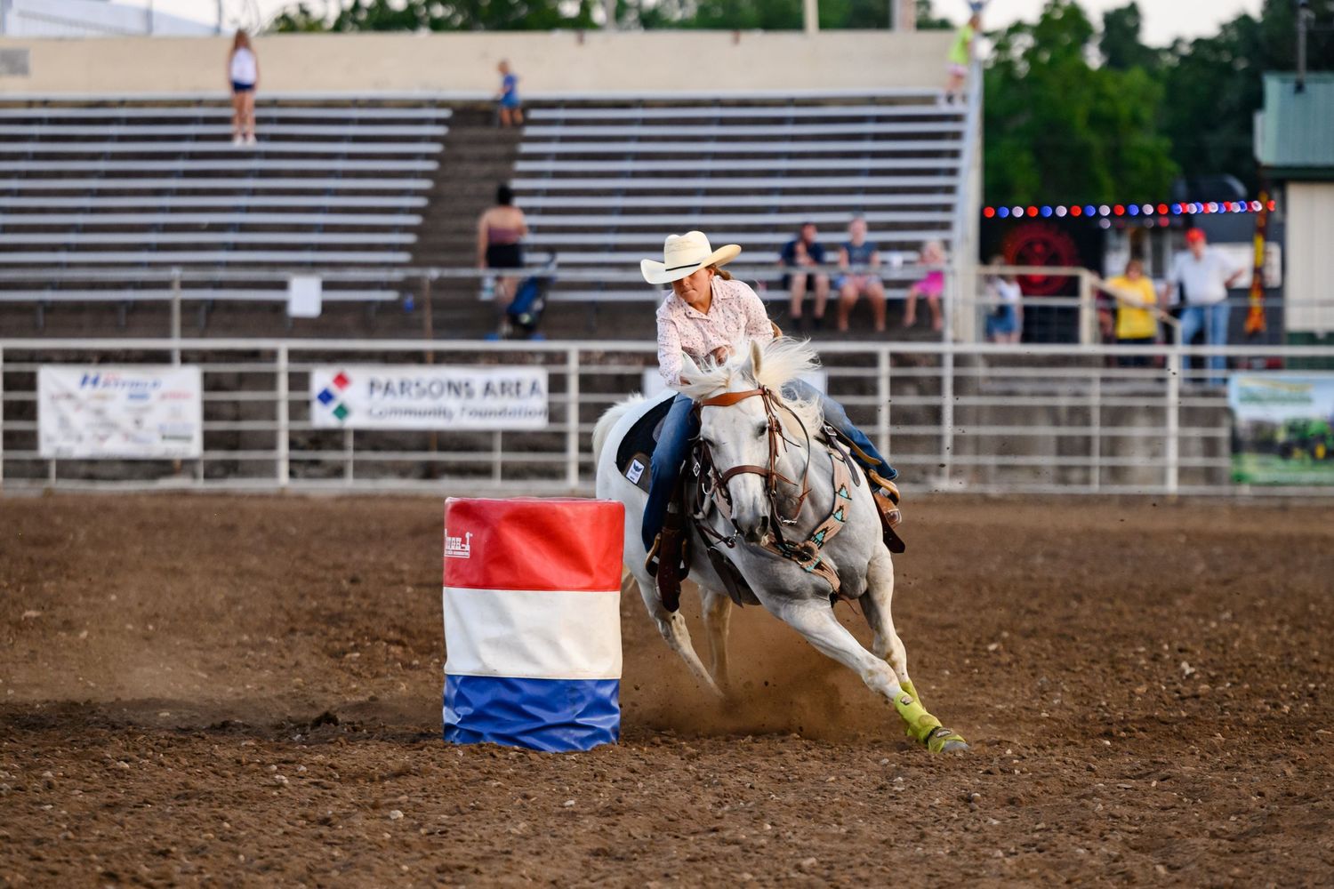 A cowgirl competes in a rodeo barrel racing event on a white horse kicking up dust in an arena at the Labette County Fair.