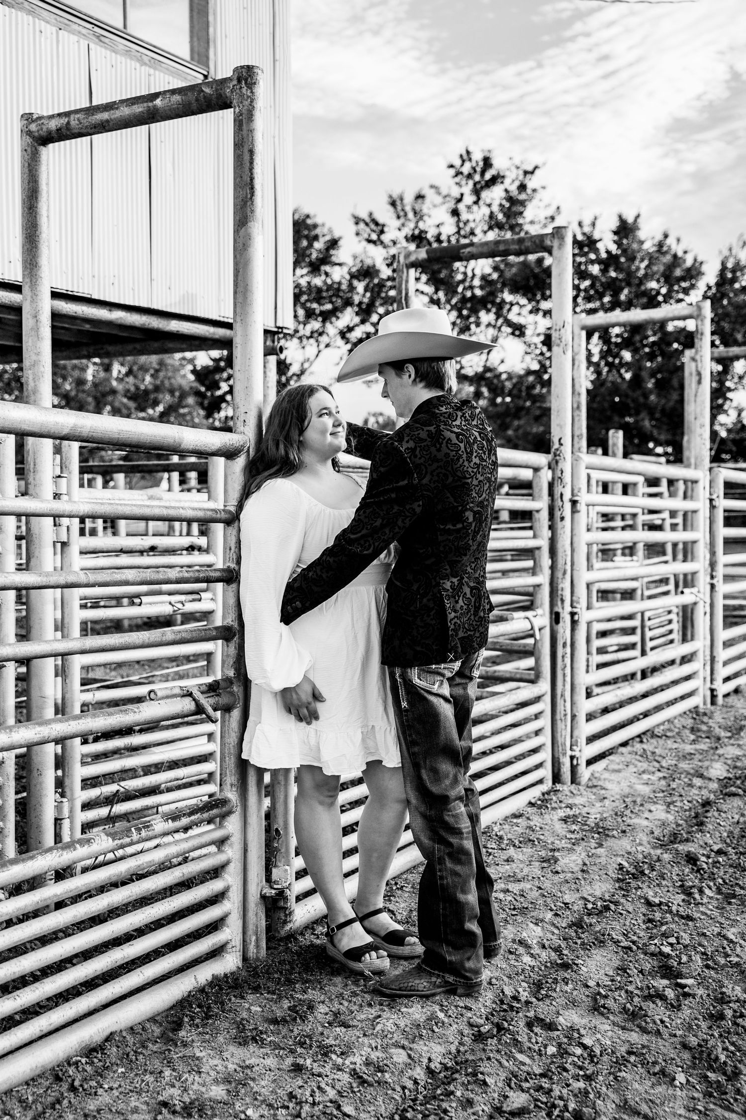 An engaged couple leaning against a white fence at a rodeo arena in Southeast Kansas.