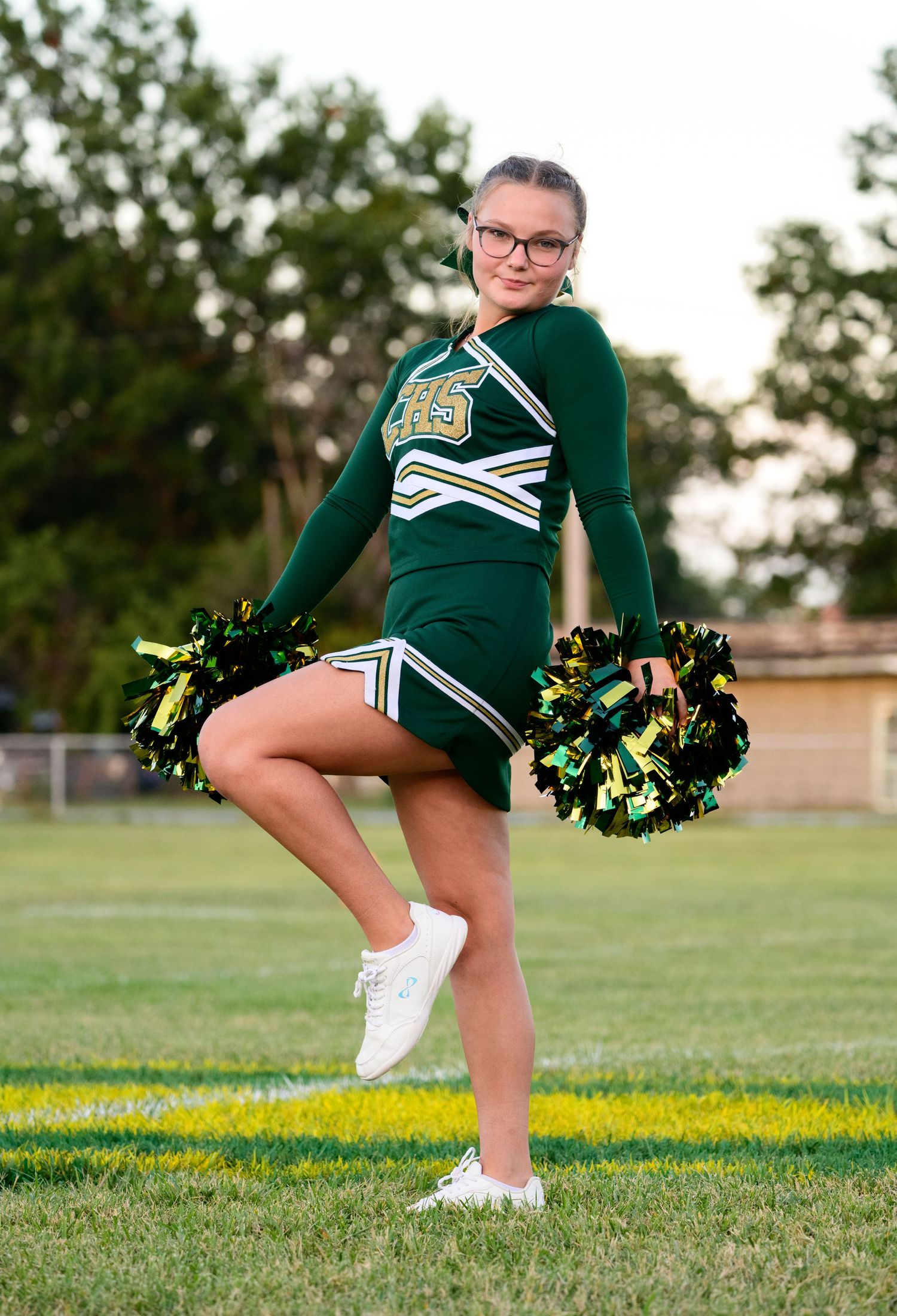 Cheerleader in green and white uniform with pom poms poses for a senior photo.