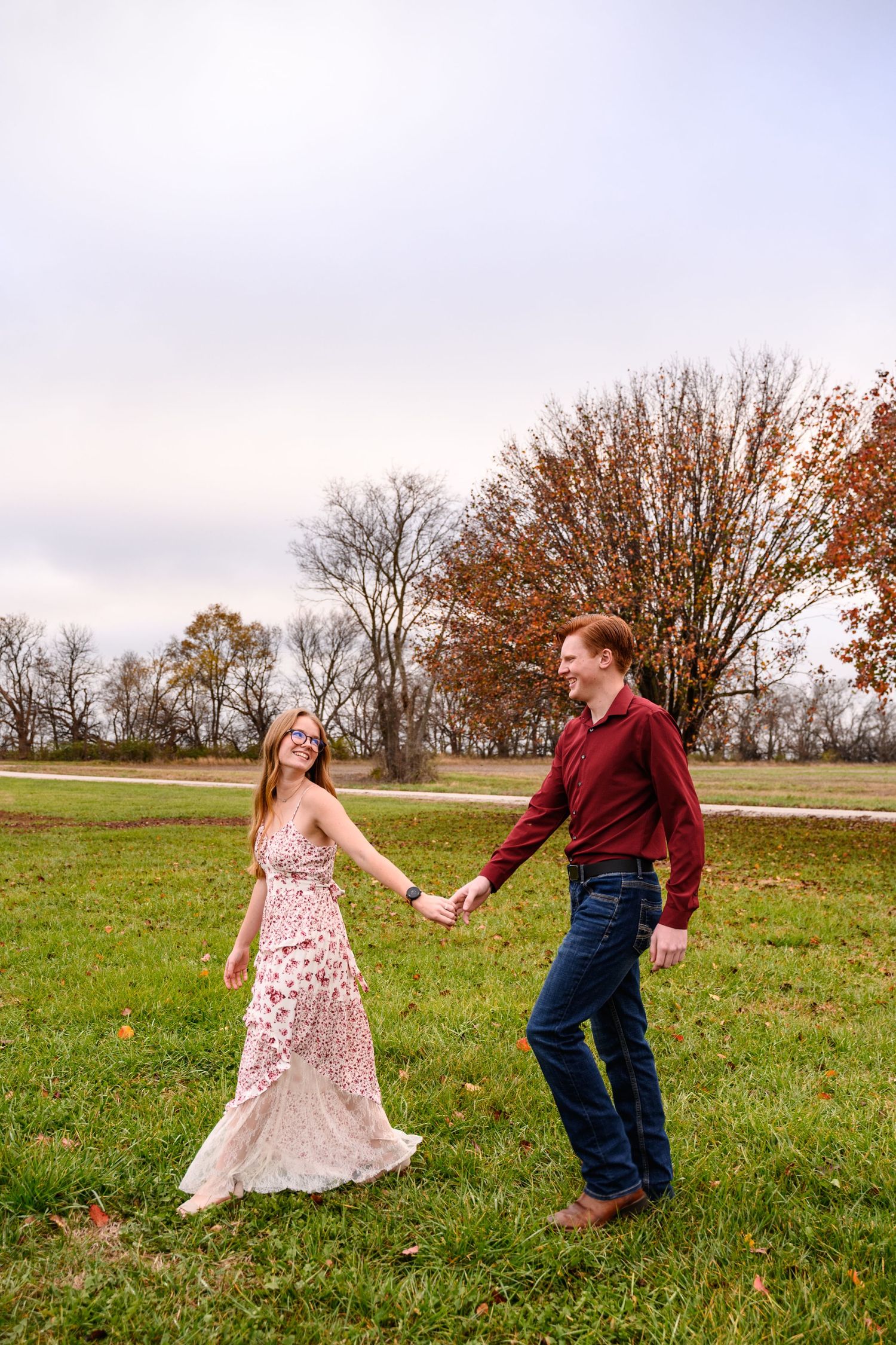 A couple dances playfully in a grassy autumn field during their engagement session.