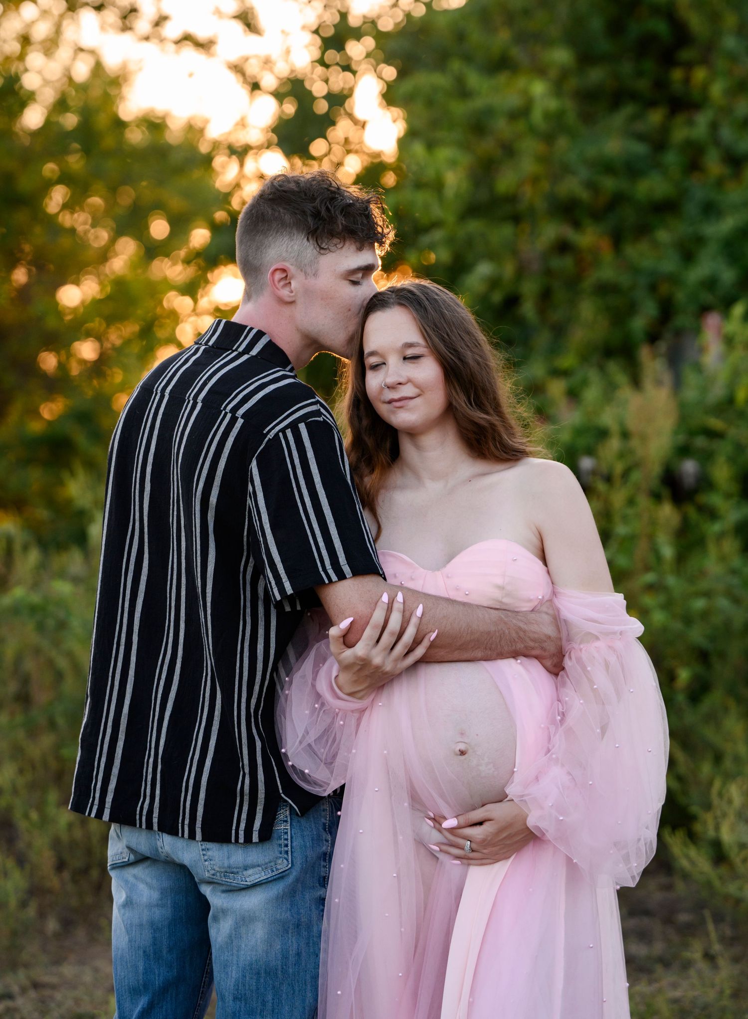 An expecting couple cuddled close in an open field in Southeast Kansas.