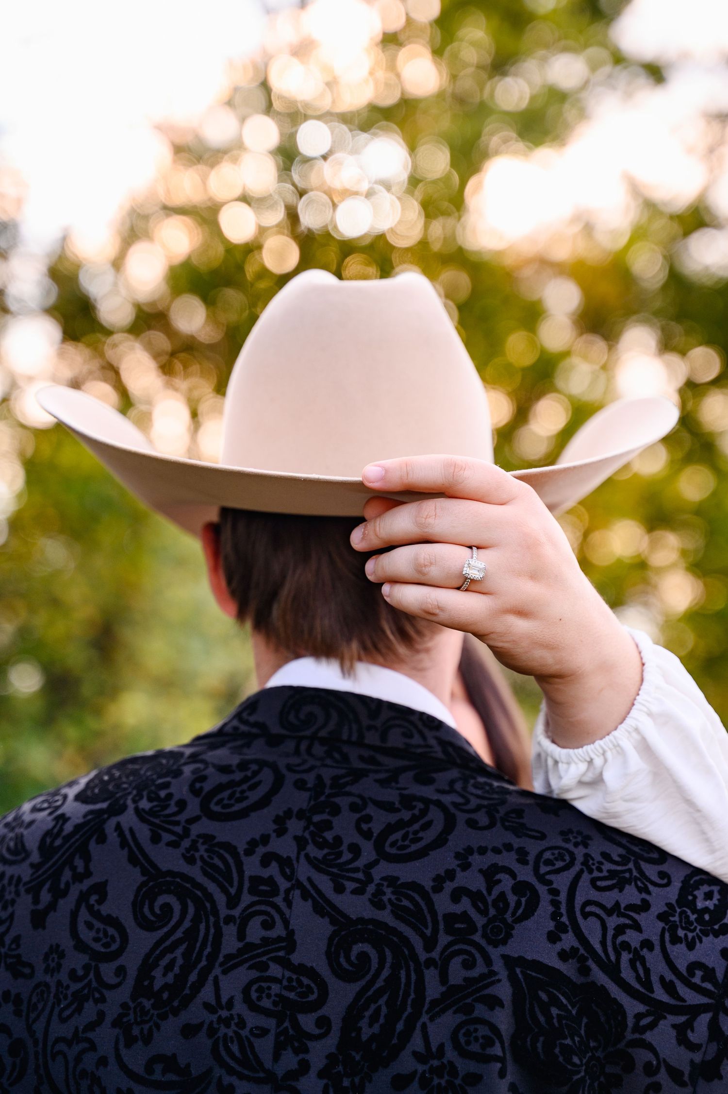 A woman holding her fiancé's cowboy hat with her hand, showing off the engagement ring.