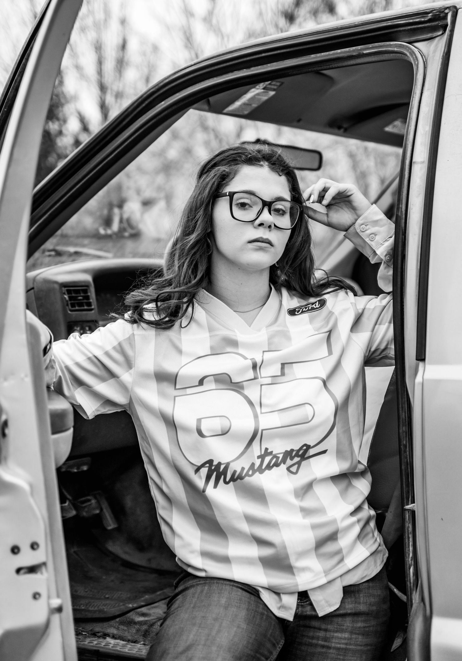 A senior girl in a Mustang jersey, leaning against an open truck door.