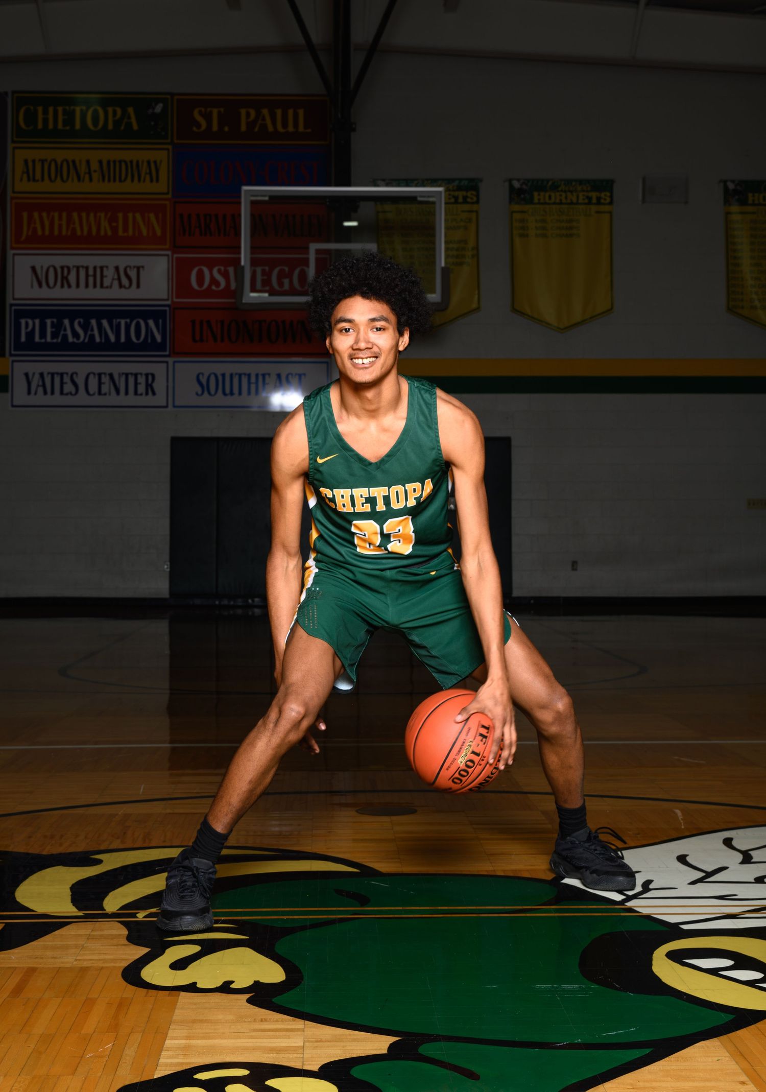 A senior basketball player in a green uniform poses on the court with a ball during a photo session.