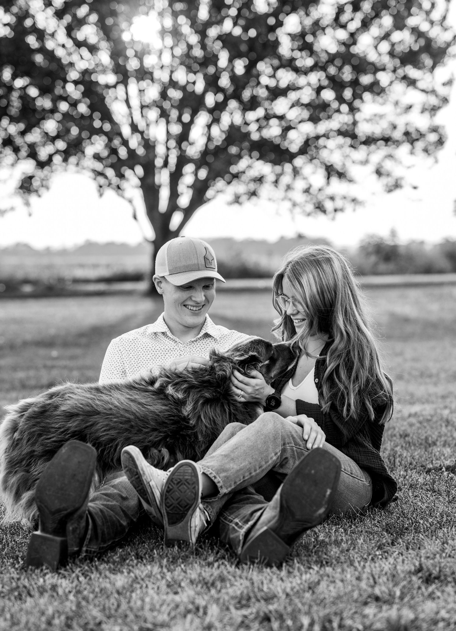 A couple is sitting on the grass with their dog.