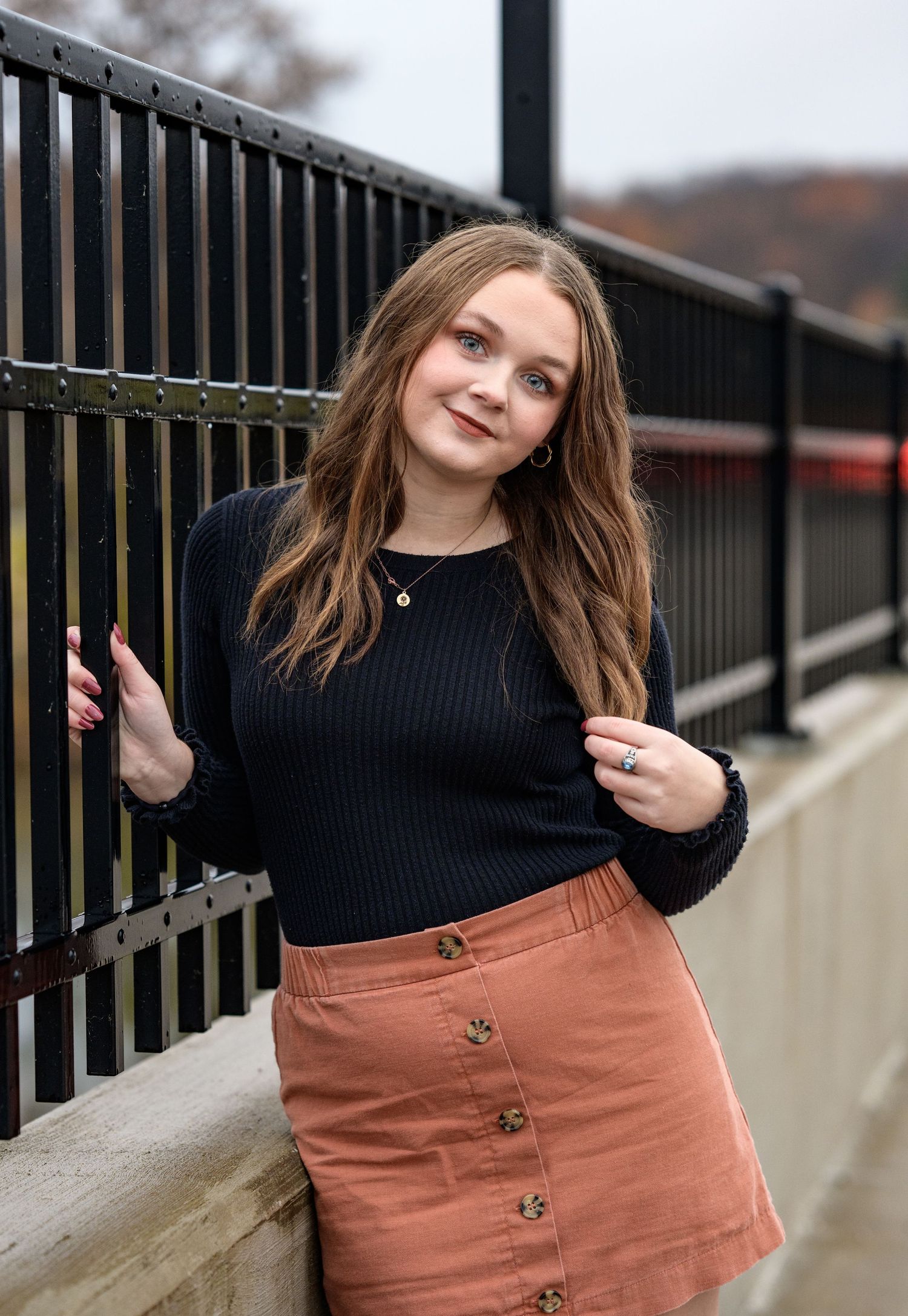 A senior girl leaning against a railing and running her fingers through her hair on a quiet street in Missouri.