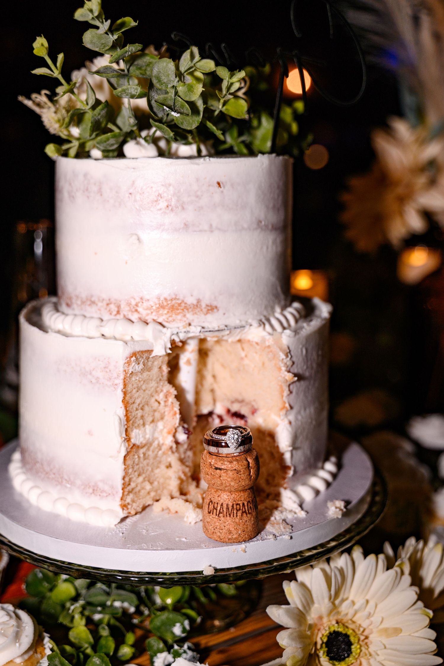 A white wedding cake with rustic floral decorations is shown being cut to reveal layers inside.