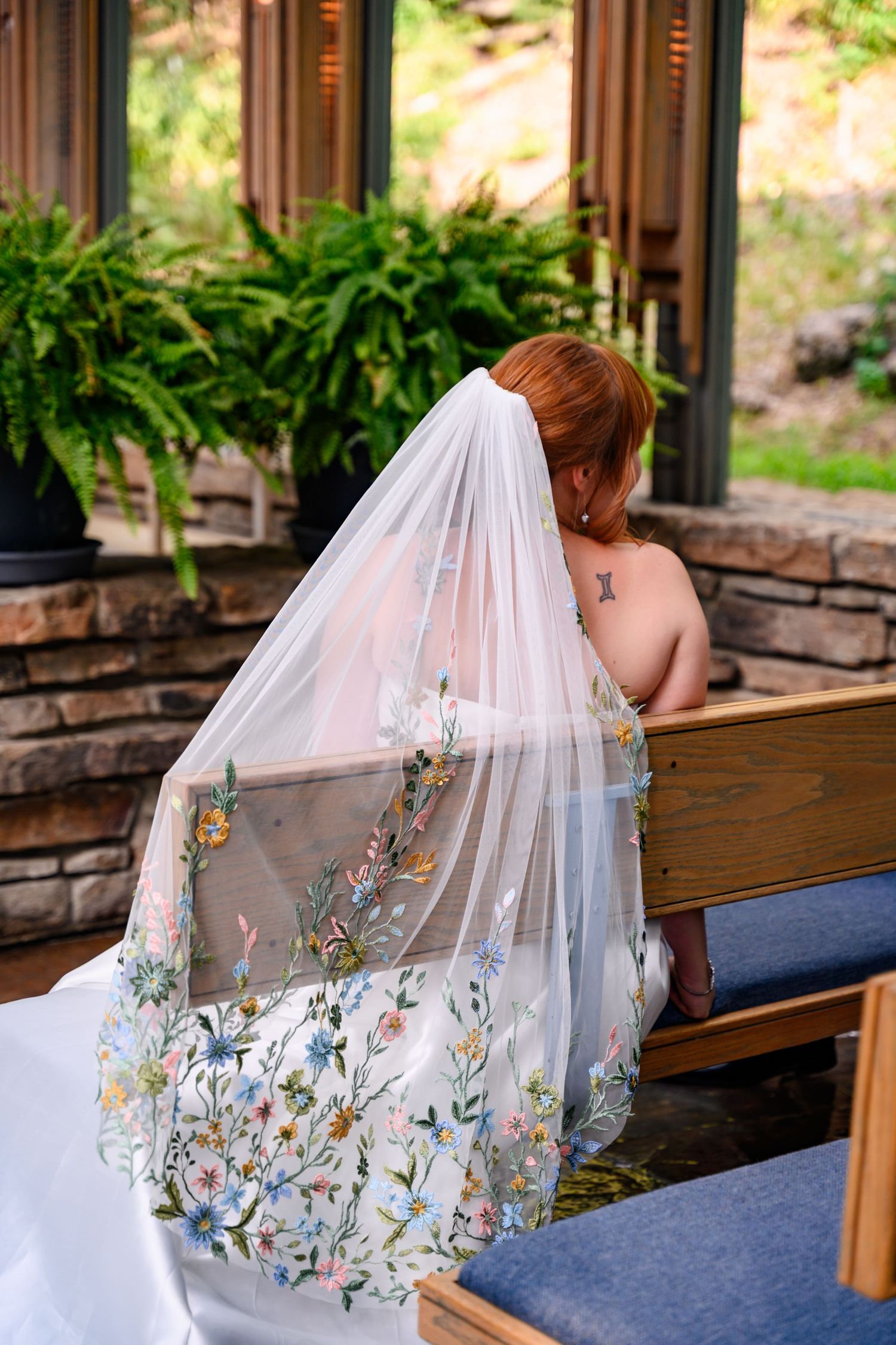 A wedding veil with delicate floral embroidery cascades over a wooden church pew in natural lighting.
