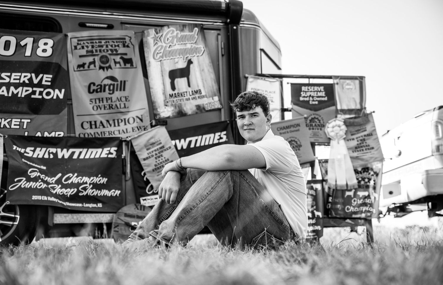 A Kansas senior sitting in front of a trailer with champion banners from all of his years showing livestock.