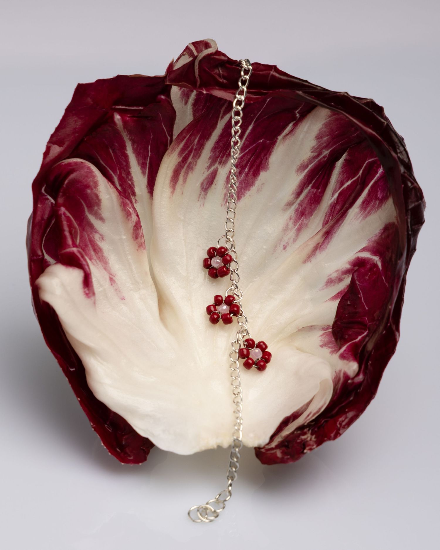 A sequence of five images showing radicchio leaves being transformed into decorative jewelry with gemstone accents.
