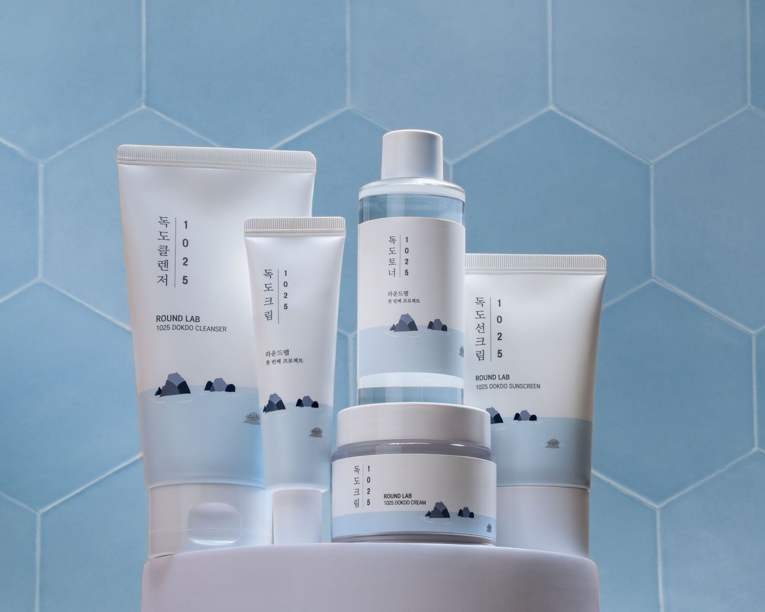 White skincare product containers with minimalist design displayed against a soft blue hexagonal tile background.