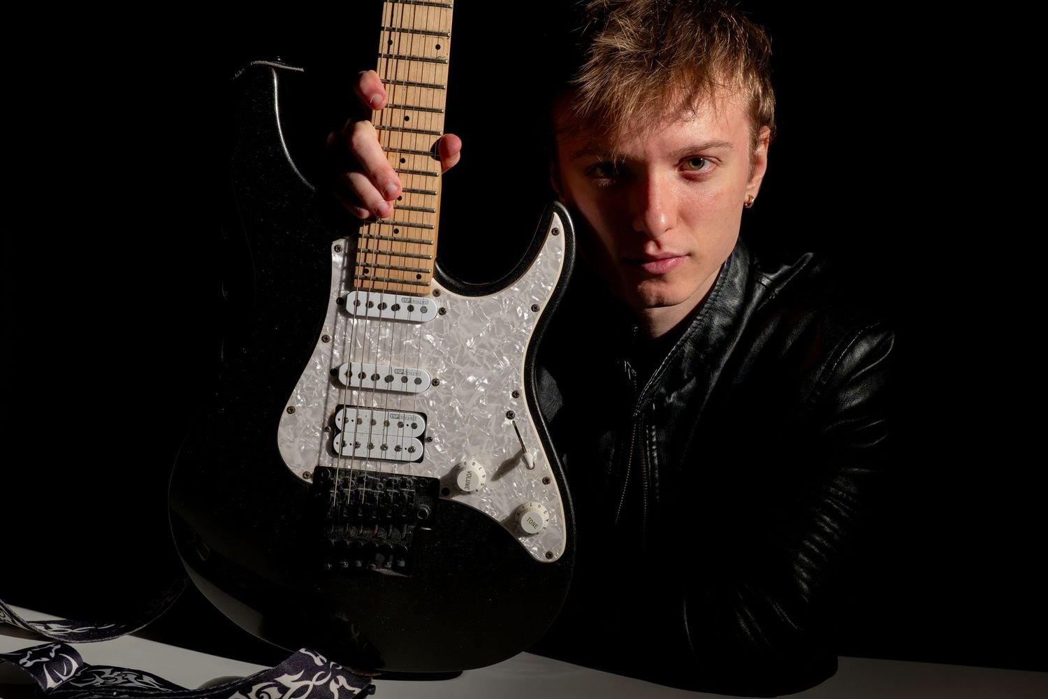 Dramatic studio portrait of musician with electric guitar against dark background.