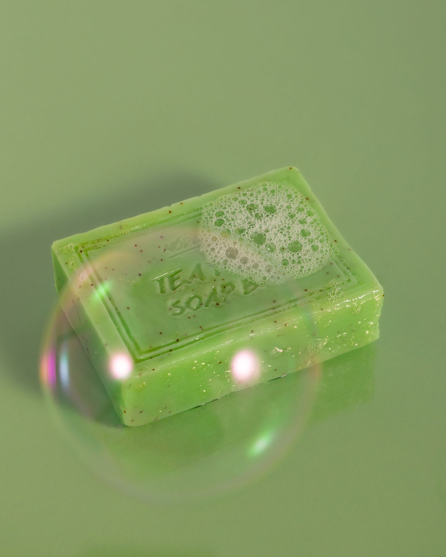 A green translucent bar of soap with bubbles photographed against a mint background with light reflections.